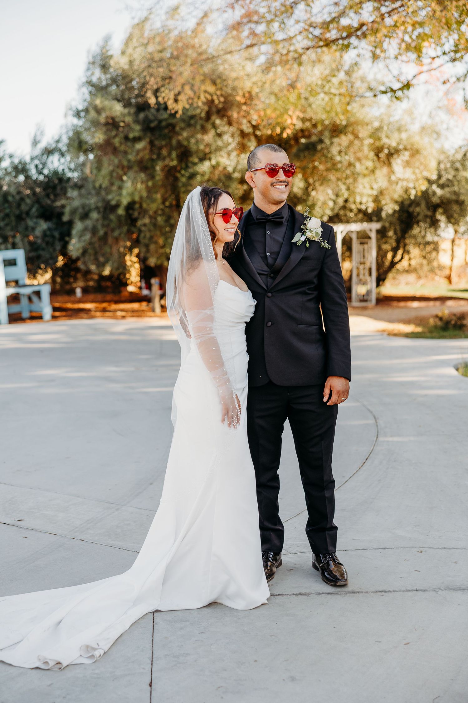 Wedding couple walking together on a concrete path with sunlit trees in the background.
