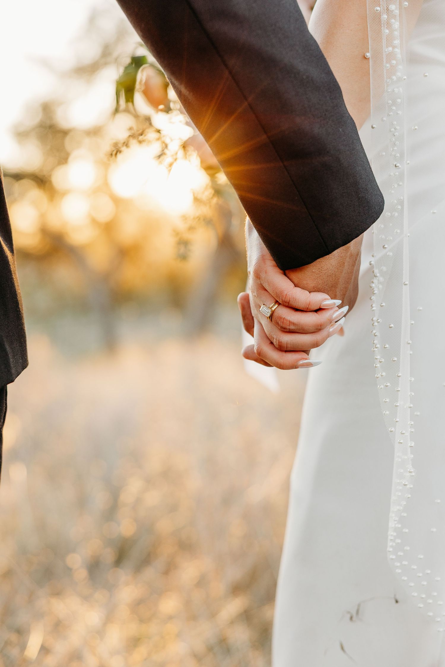 Close-up of bride and groom's hands during outdoor wedding ceremony with golden sunlight.