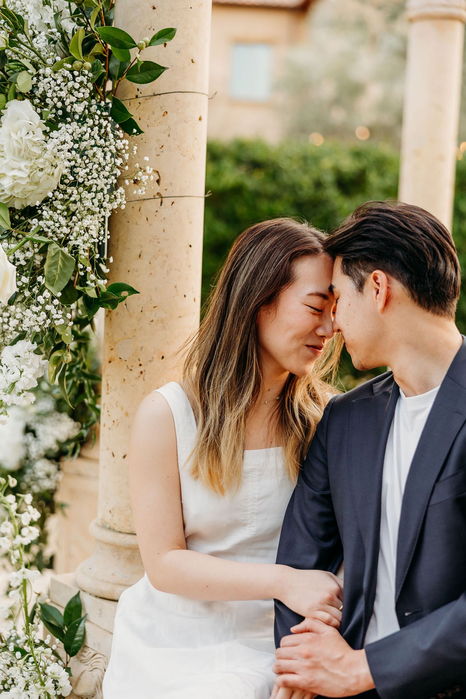 Intimate close-up moments shared in a garden setting with white floral arrangements.