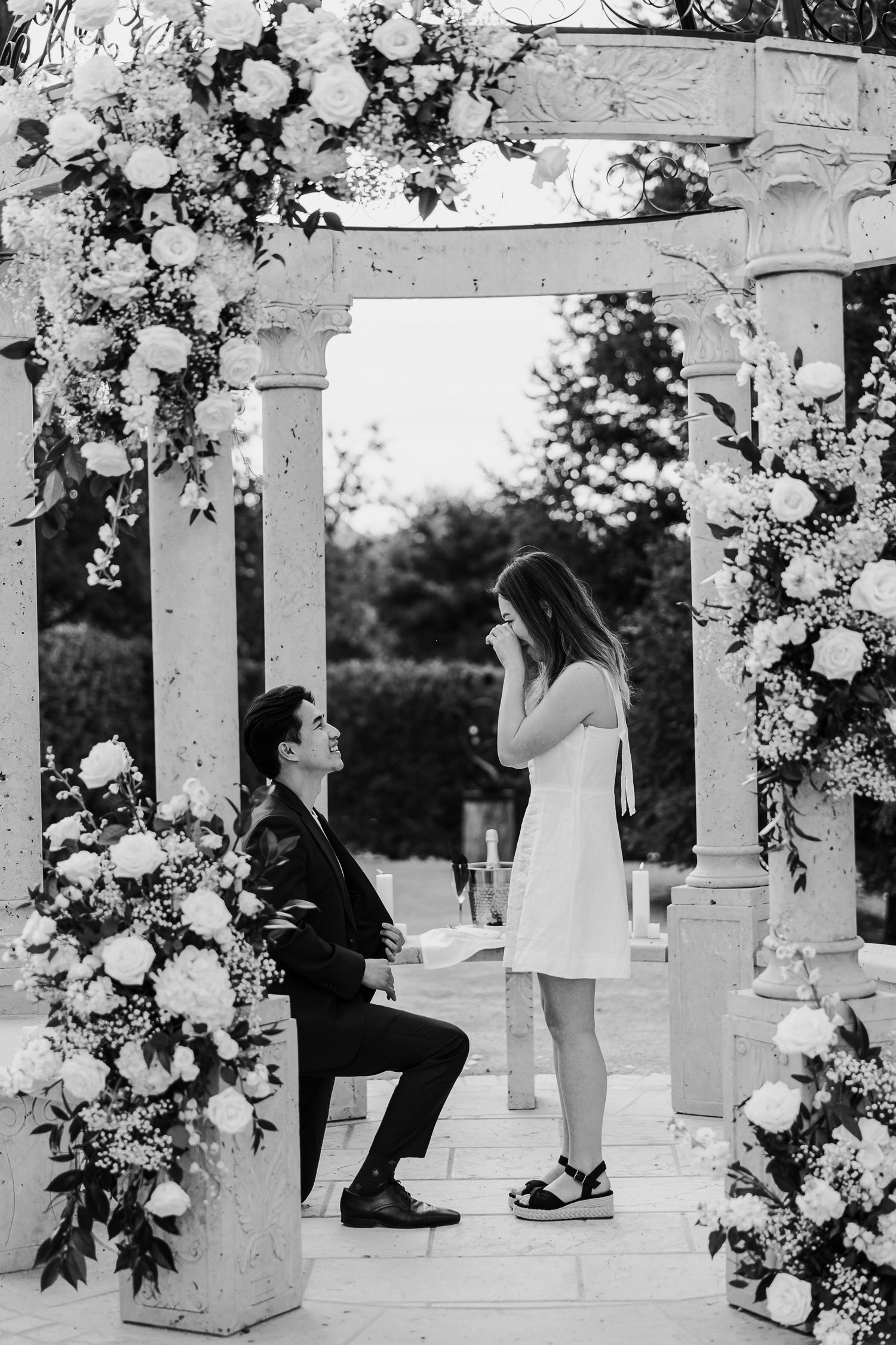 A romantic proposal scene under a white pergola decorated with floral arrangements.