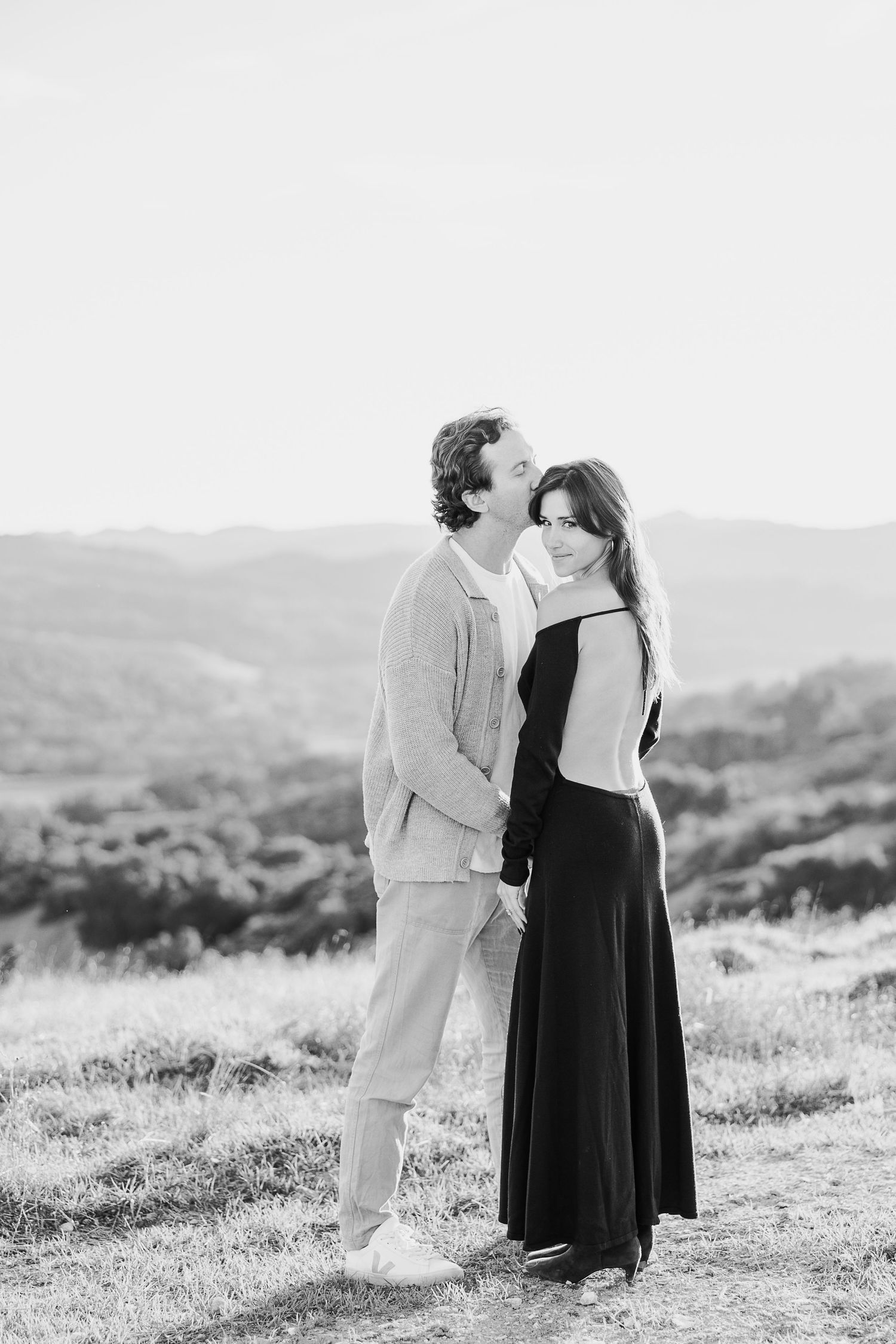 A couple shares romantic moments in a scenic outdoor setting captured in black and white photography.