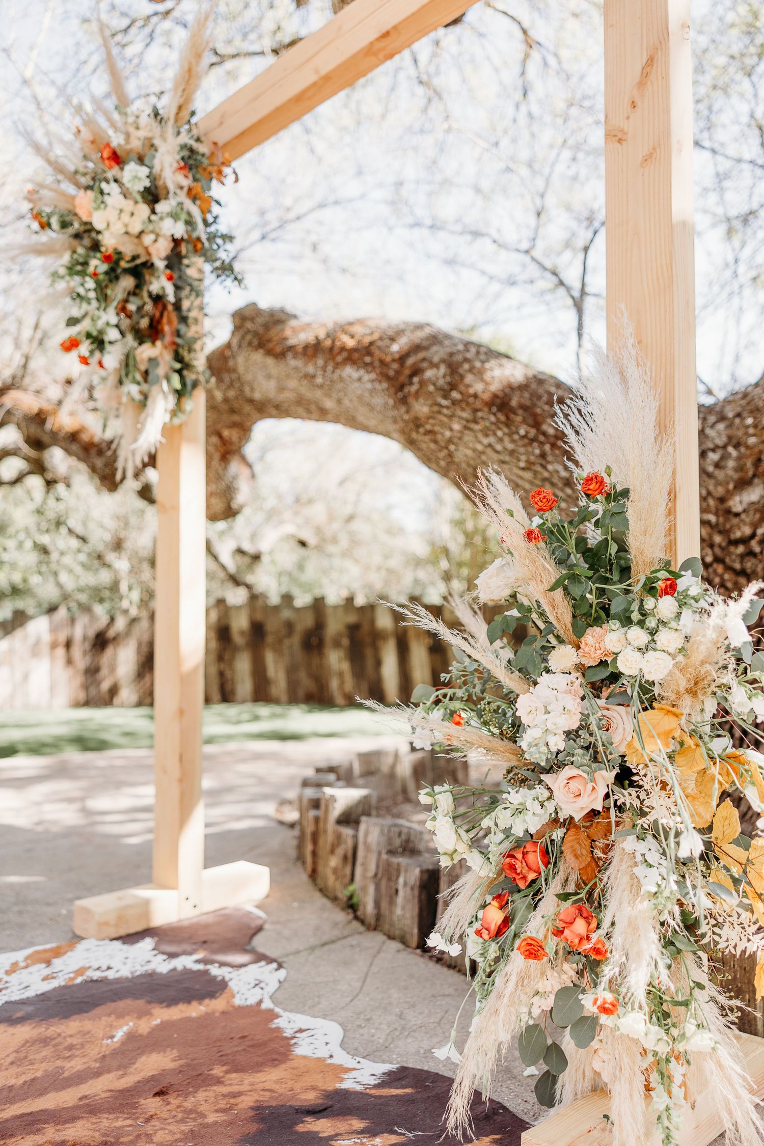 Rustic wooden wedding arbor decorated with peach and white floral arrangements under oak trees.