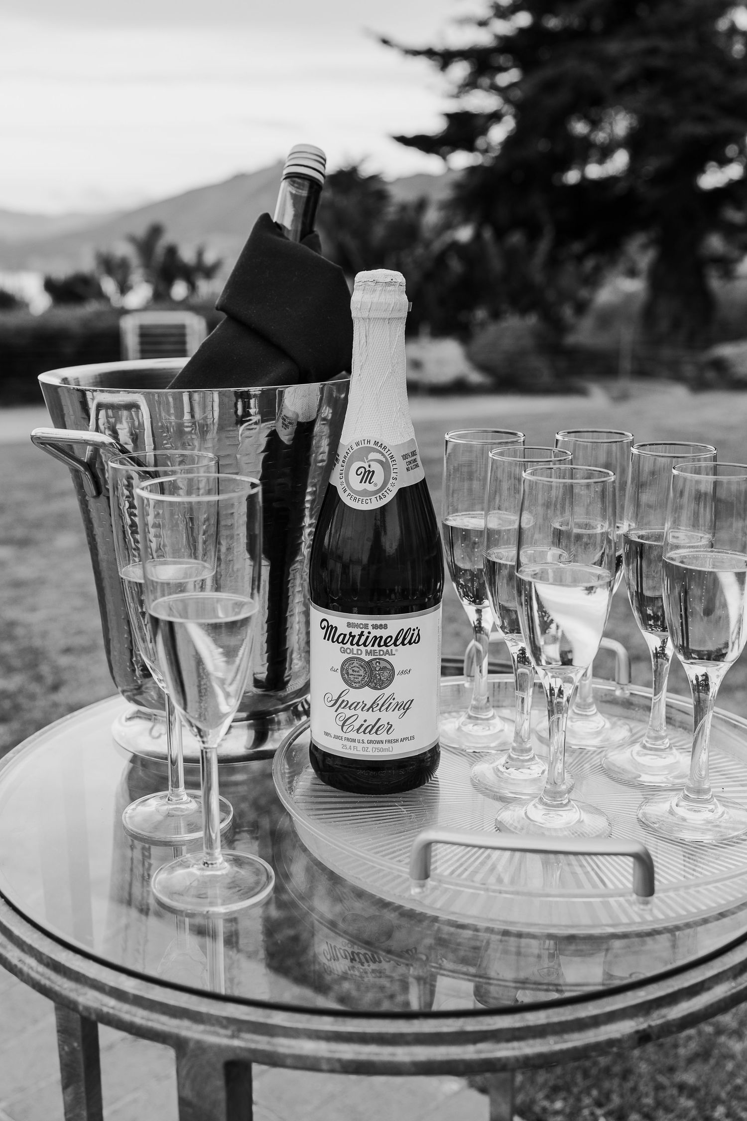 Elegant champagne glasses and bottles arranged on round glass tables for an outdoor celebration event.