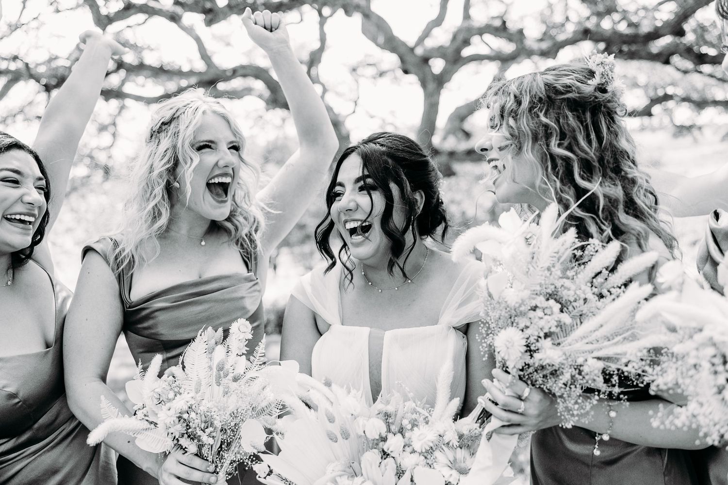 Black and white photo of bridal party laughing and sharing a candid moment outdoors.
