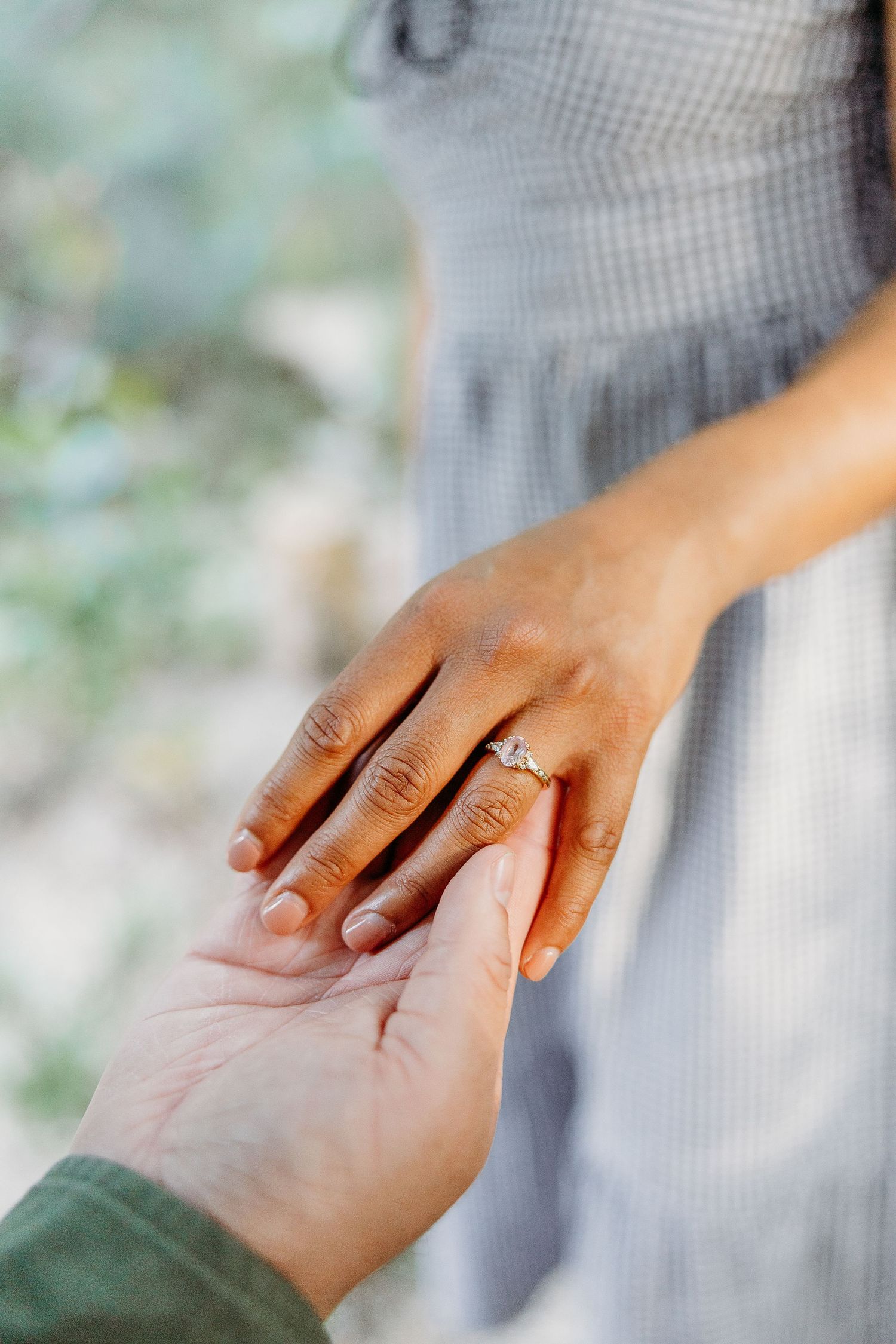 Close-up view of hands with engagement ring showing proposal or romantic moment against soft blurred background.