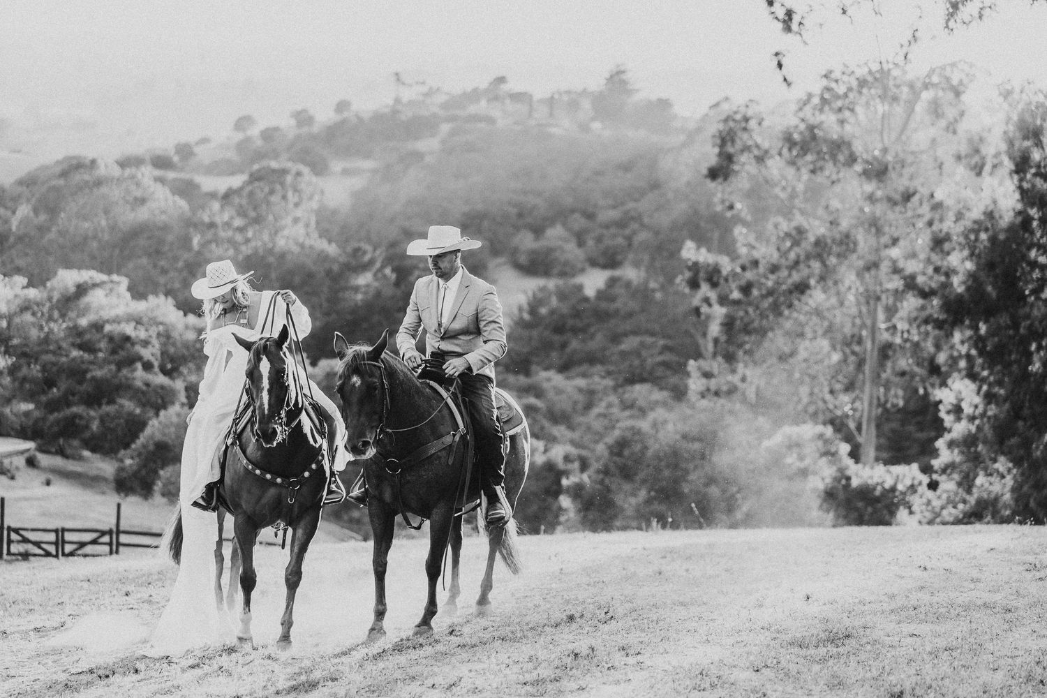 Black and white photo of two people riding horses on a mountain path.