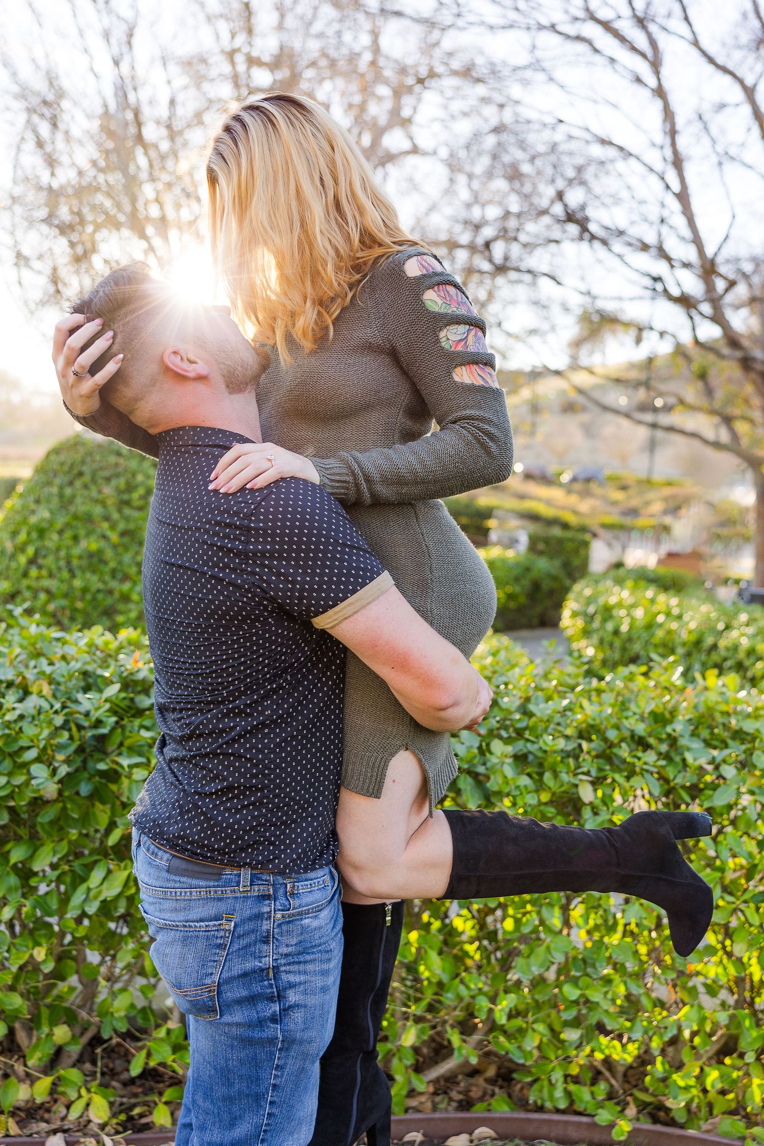 A tender moment between a couple as one lifts the other against a sunlit garden backdrop.