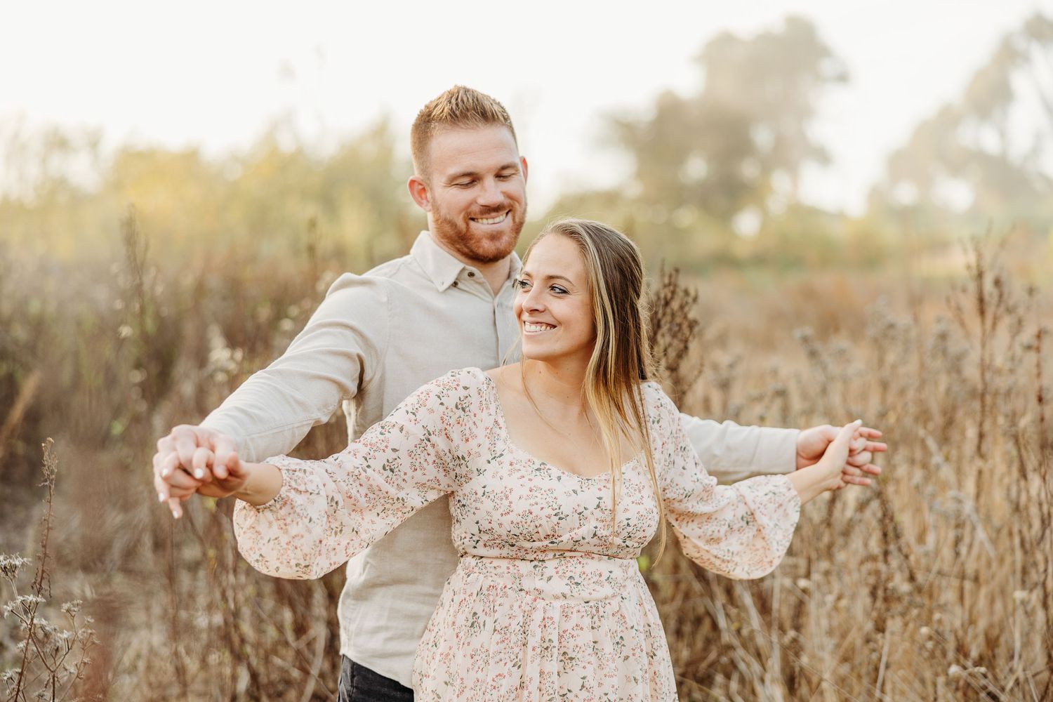 Joyful couple dancing and laughing together in a sunlit meadow during golden hour.