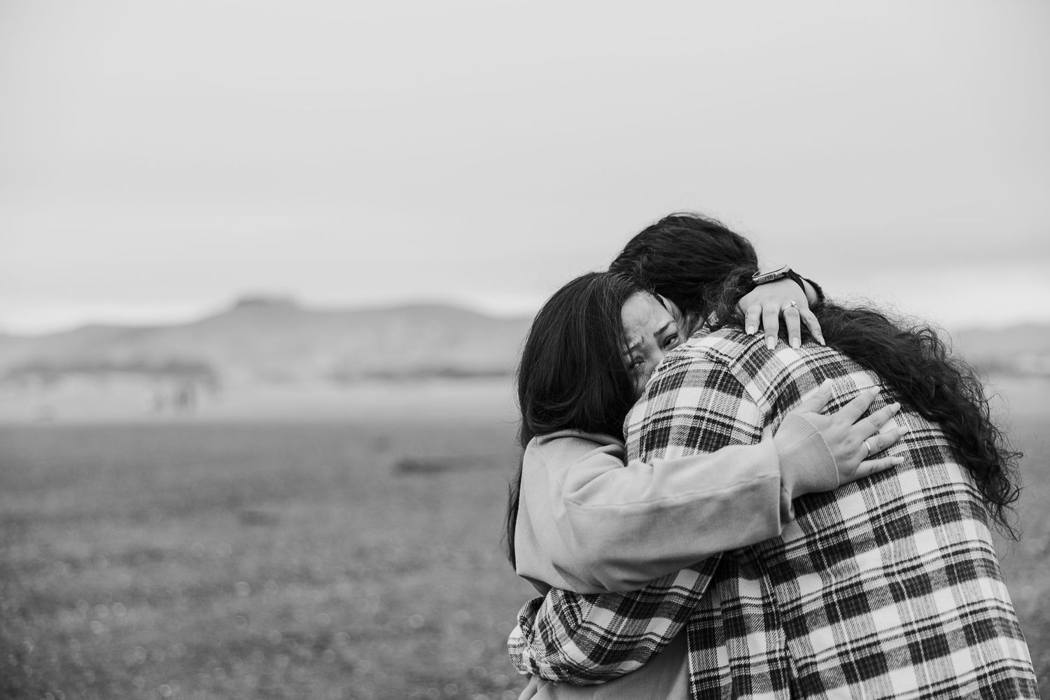 Two people sharing an emotional embrace in black and white against a misty rural landscape background.