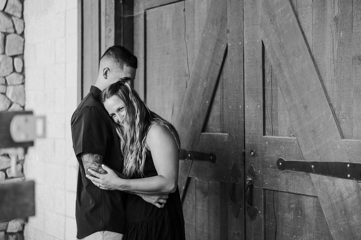 Black and white photo showing a rustic wooden barn door with stone wall details.