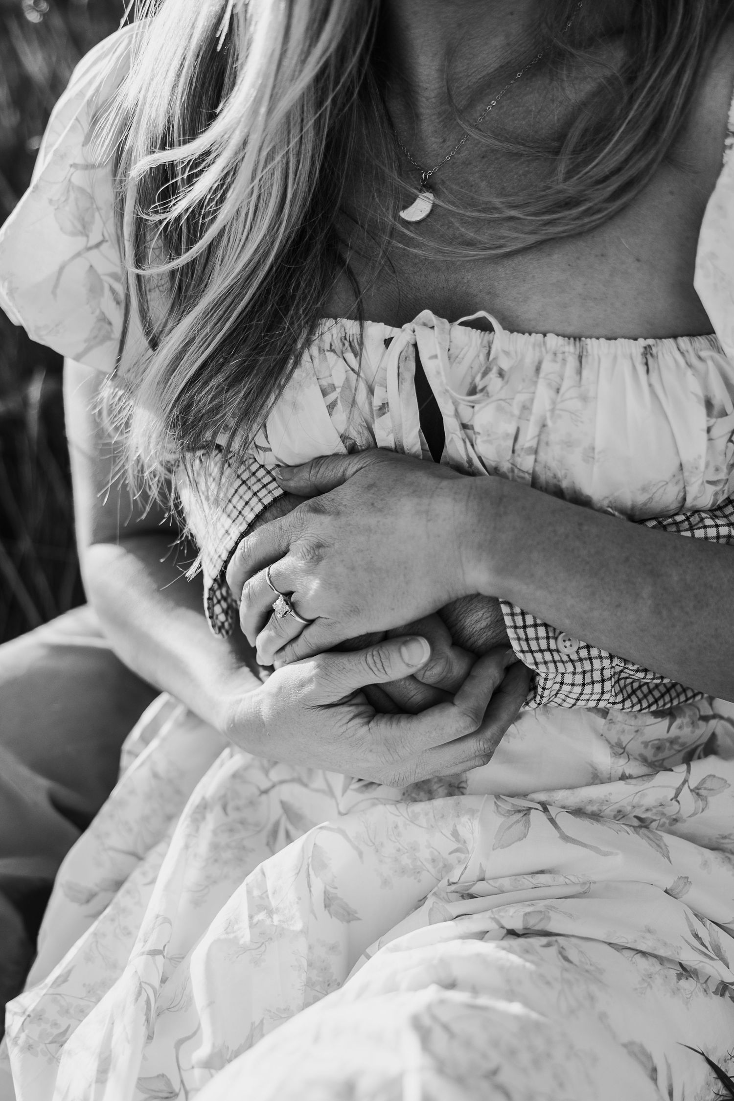 Black and white close up of hands gently resting on a white dress with delicate details.