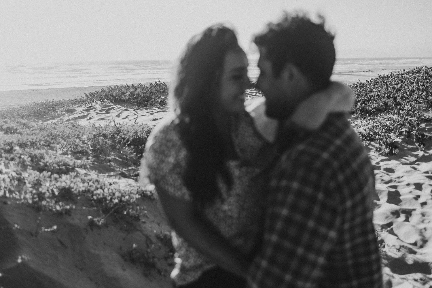 Black and white portrait of couple sharing intimate moment on coastal shore.