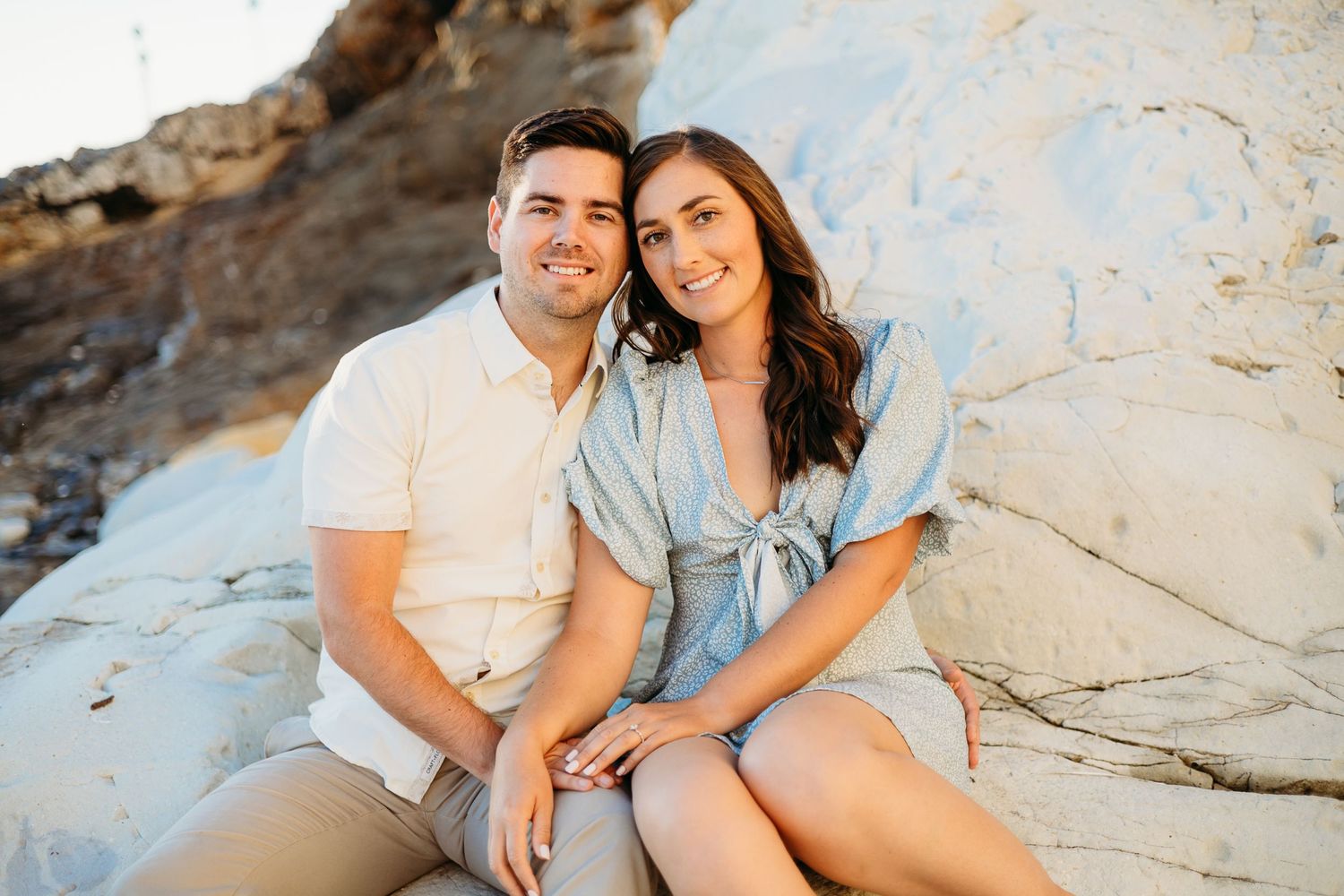 A couple sits together on white rocks during a sunny outdoor photoshoot.