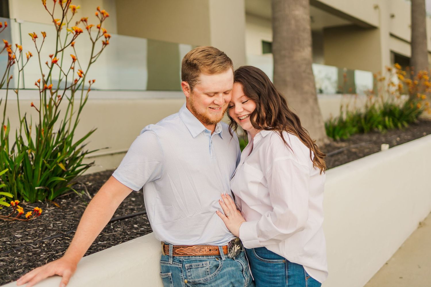 Couple in casual attire sharing an intimate moment against modern building exterior.