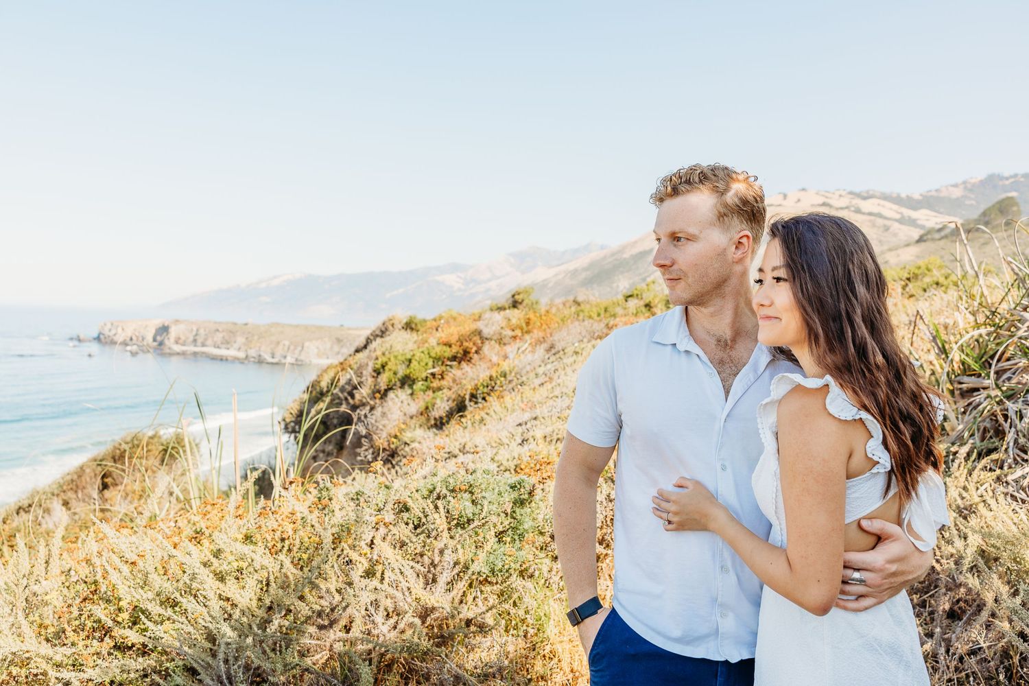 Couple enjoying scenic coastal view in complementary white and blue outfits.
