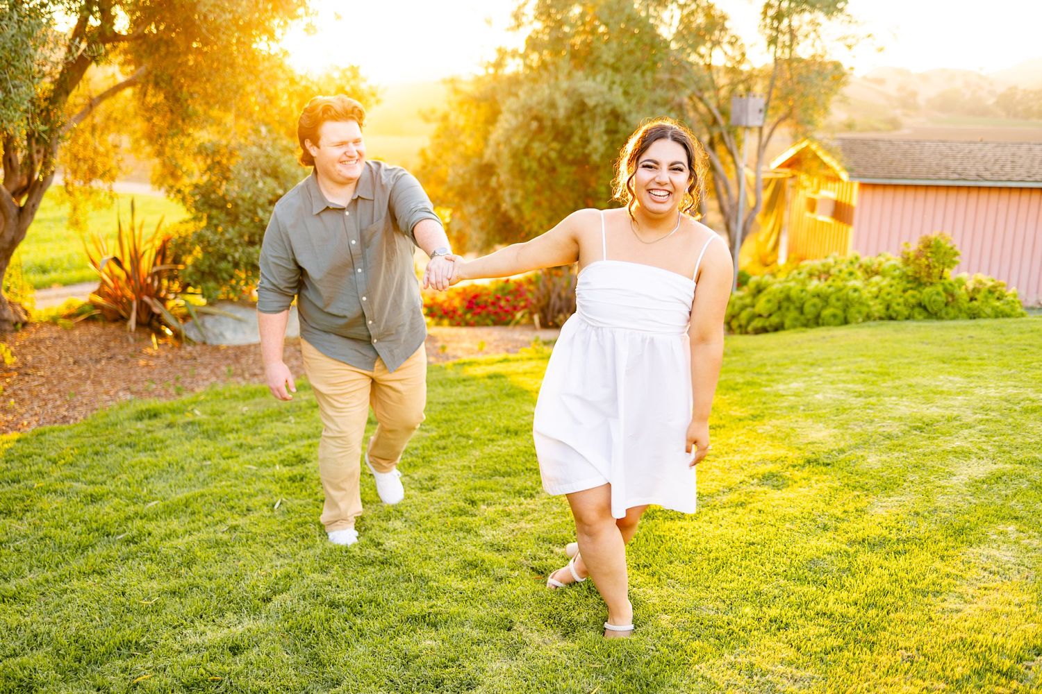 Playful couple running together on grass during golden hour in garden landscape.