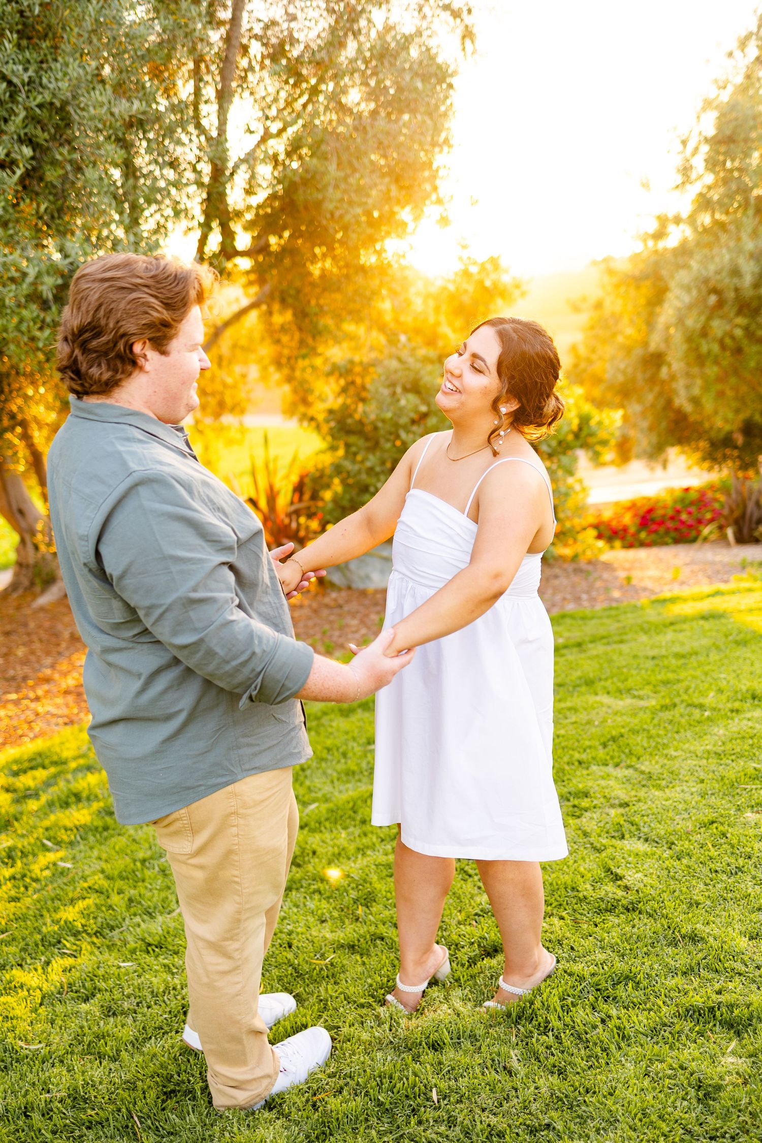 Couple dancing together on grass during golden sunset in peaceful garden setting.
