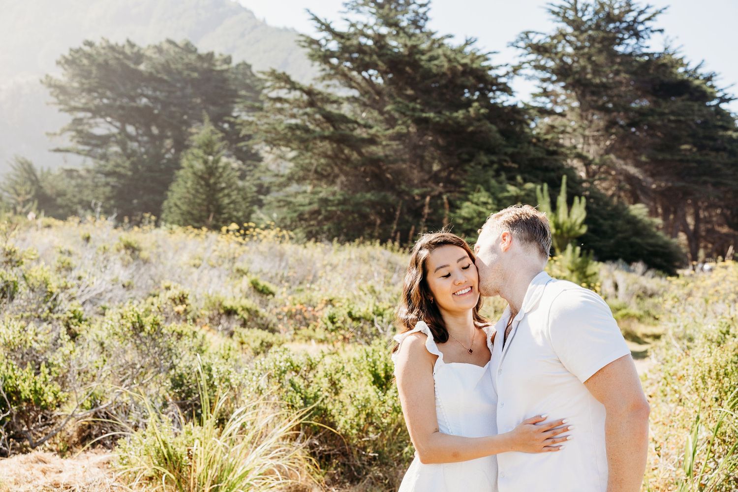 Sun-drenched portrait of couple embracing in coastal landscape.