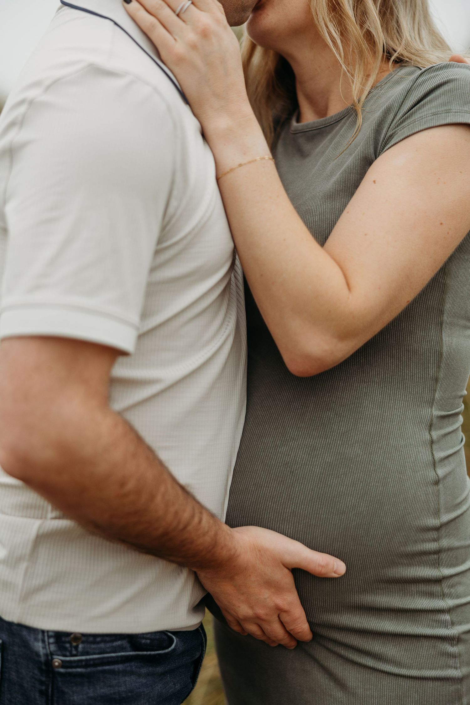 Close up shot of expectant couple embracing in casual attire against neutral background.
