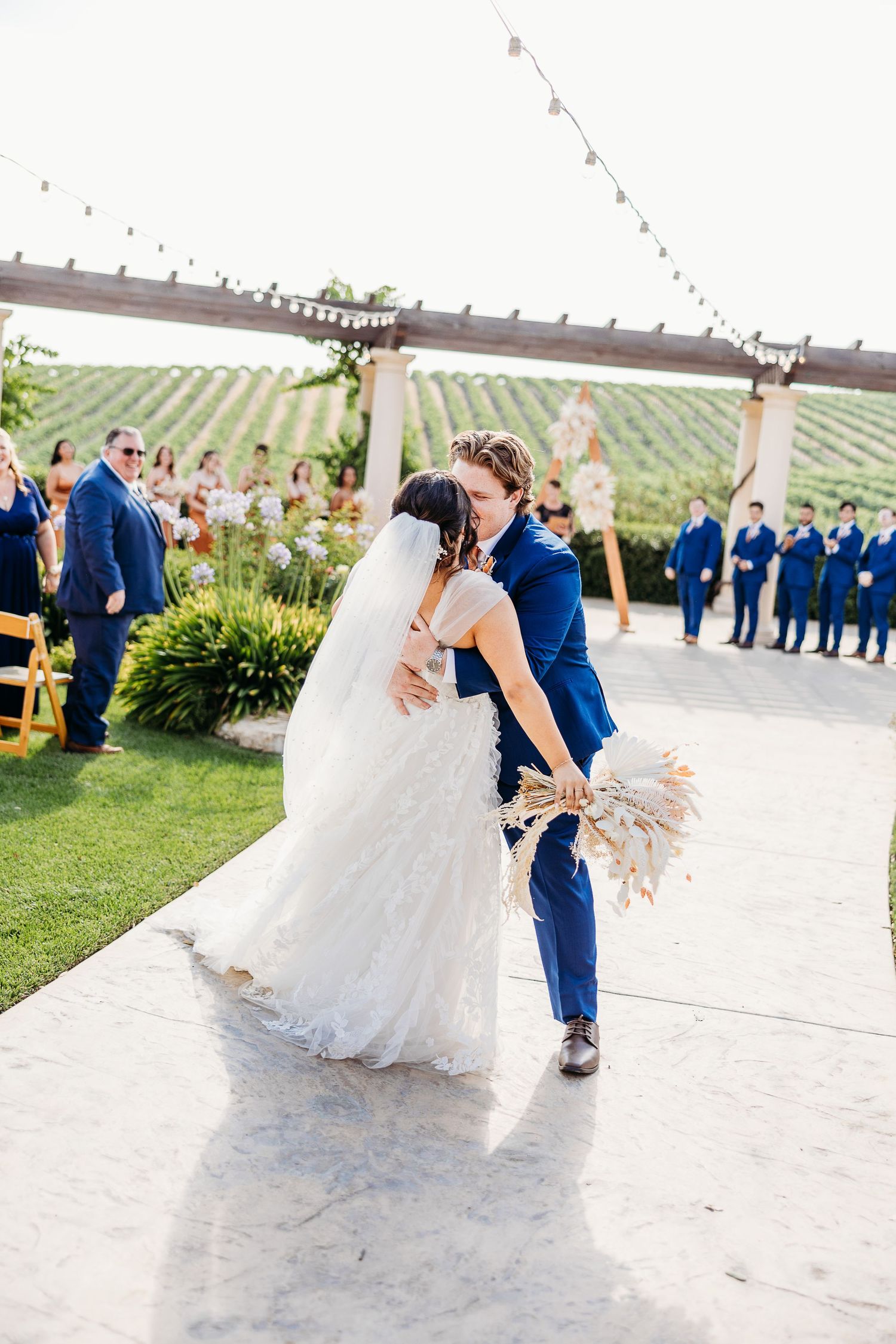 Romantic kiss shared between couple on their wedding day with vineyard hills in background.