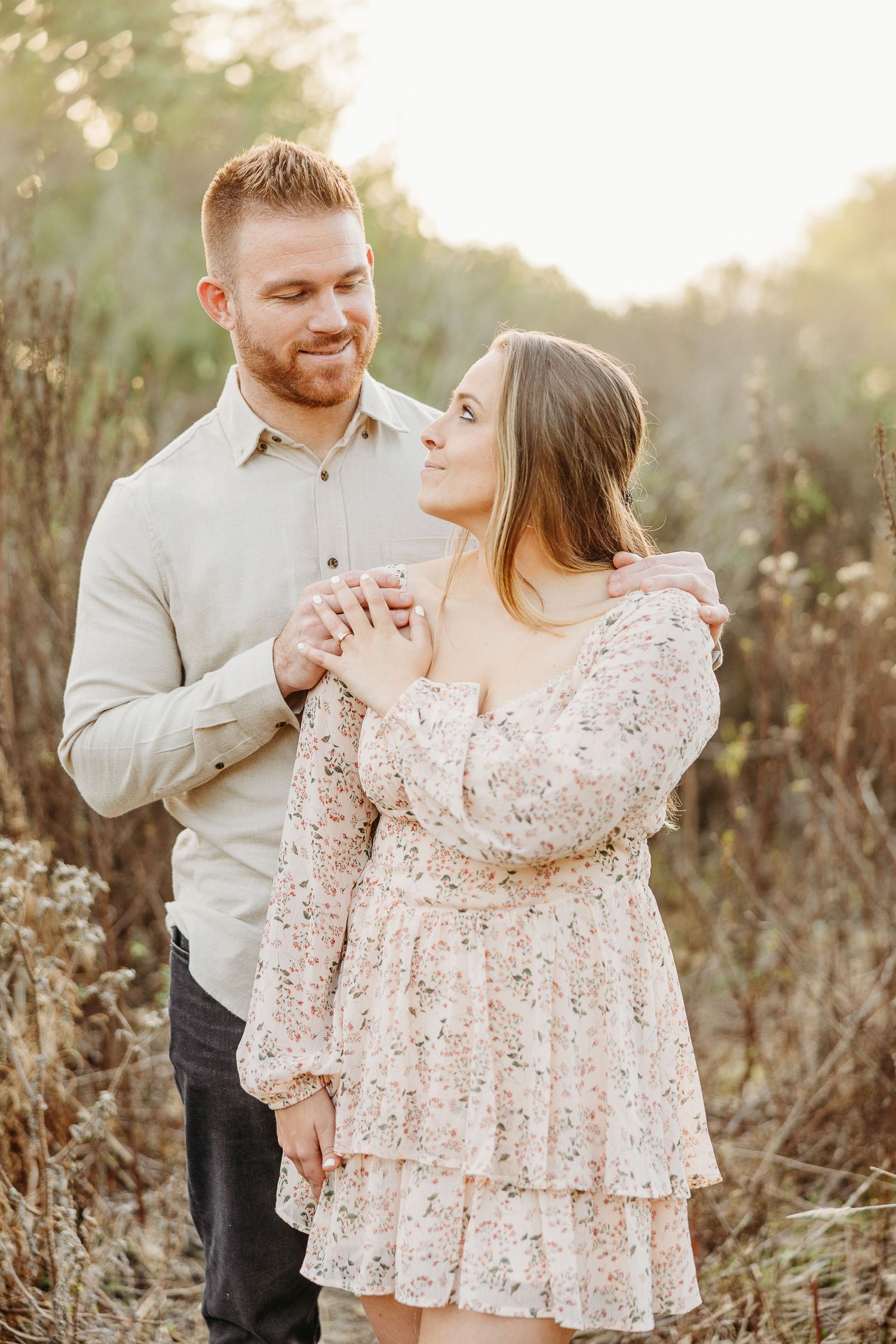Couple shares an intimate moment in a natural field setting with warm golden light.