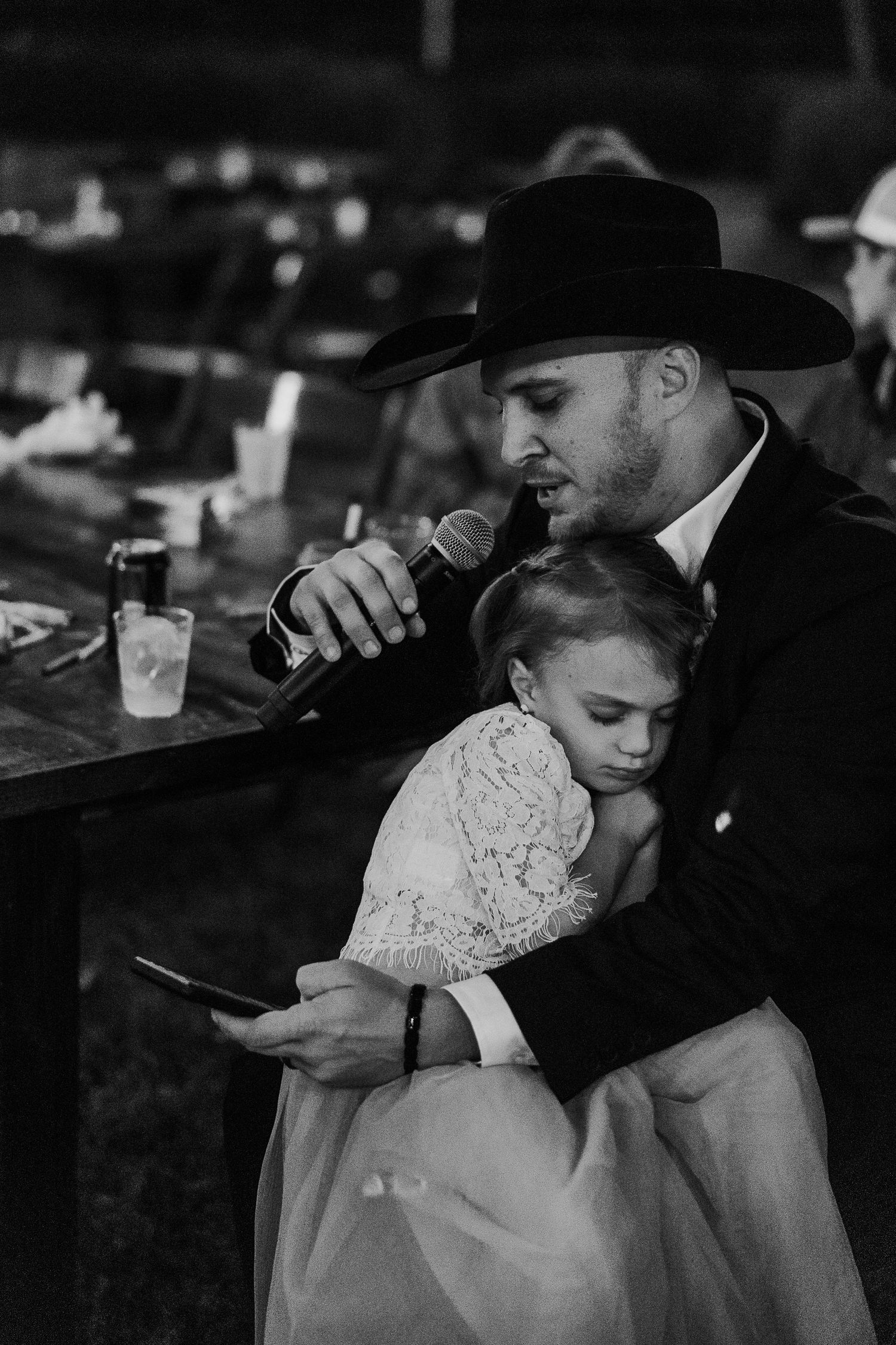 Sweet moment during reception as person speaks into microphone while holding someone close.
