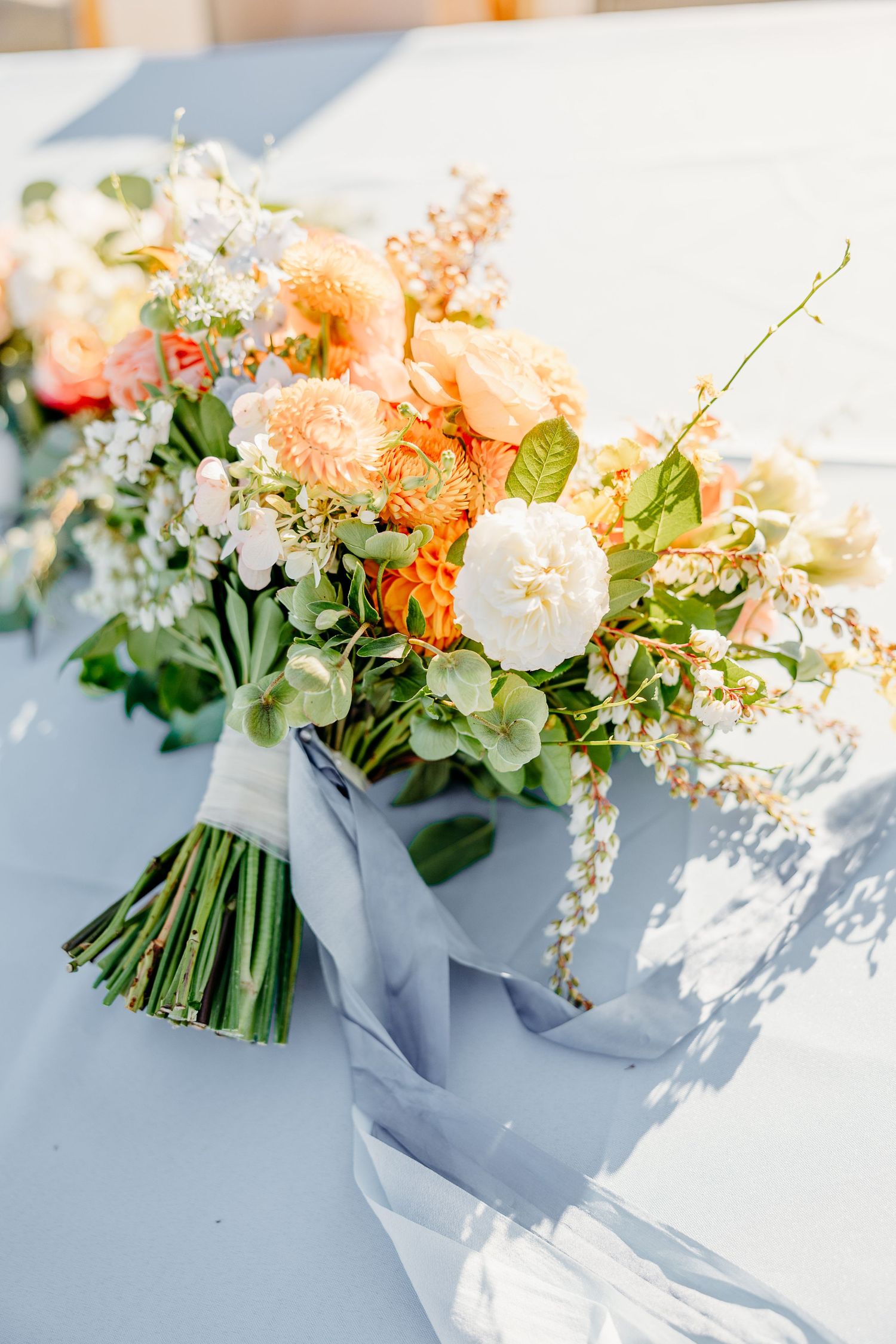 Elegant peach and white wedding bouquet with delicate flowers and sage green foliage wrapped in silk ribbon.