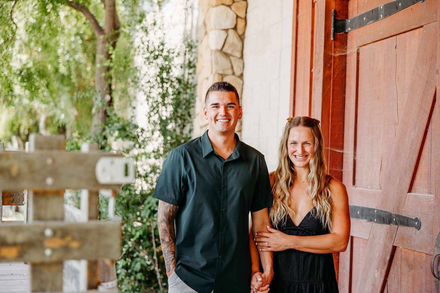 A couple shares a tender moment together while standing in front of a rustic wooden door outdoors.