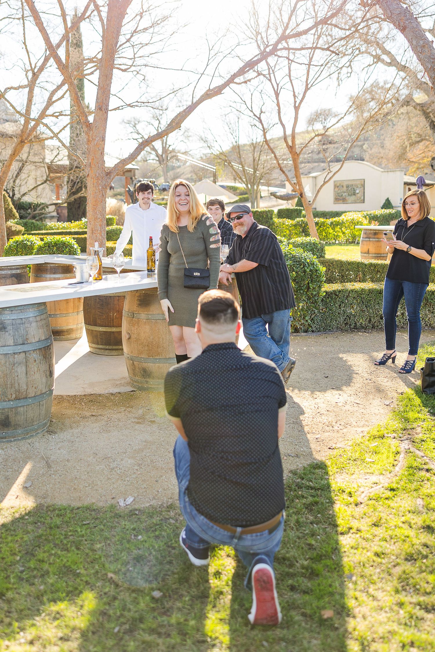A proposal moment captured at an outdoor winery setting with friends watching.