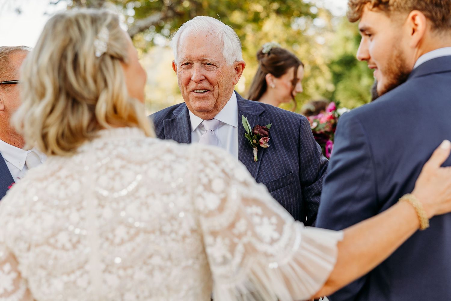 Wedding celebration outdoors with guests mingling under trees at sunset.