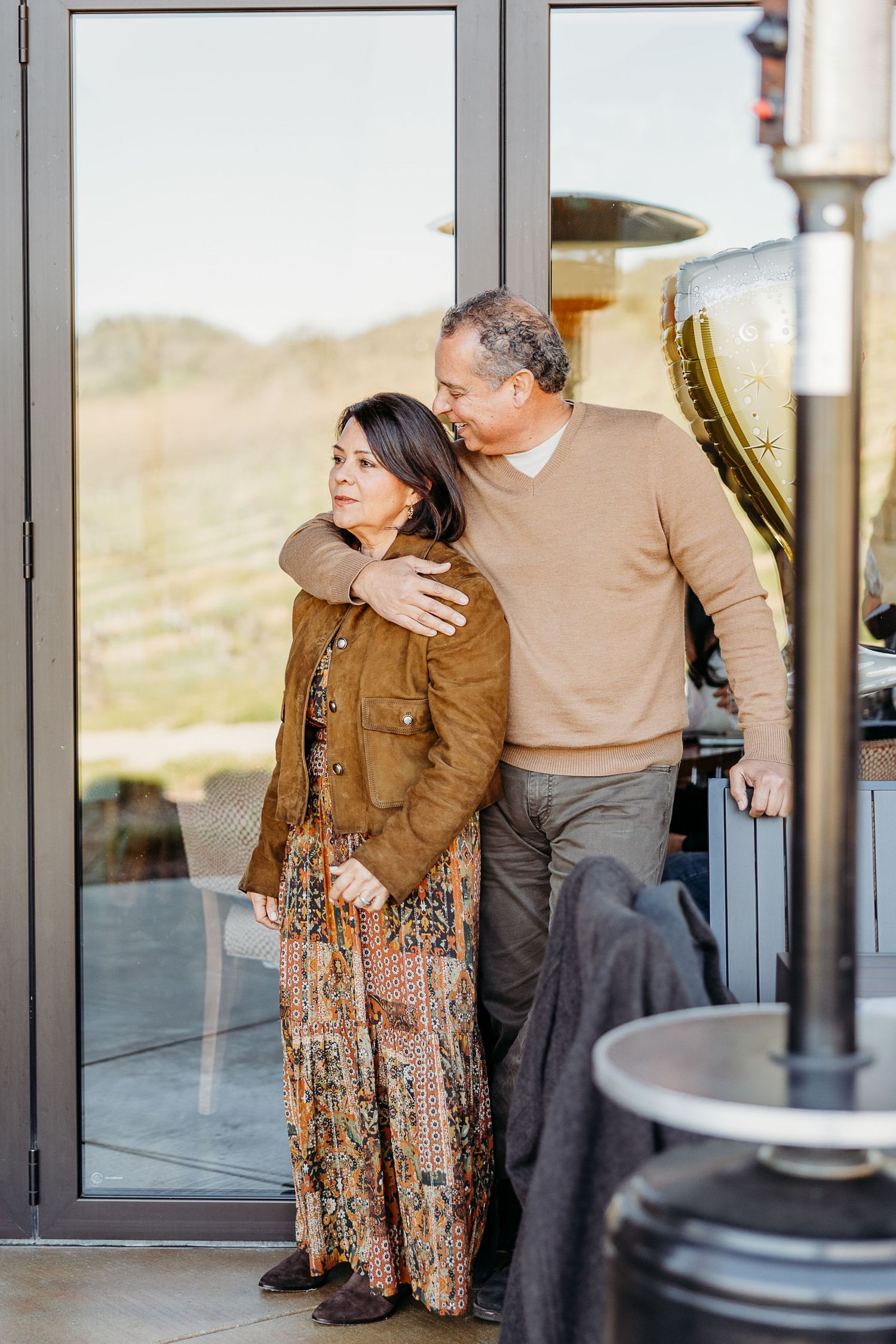 A couple dances together in front of large glass windows with natural light streaming in.