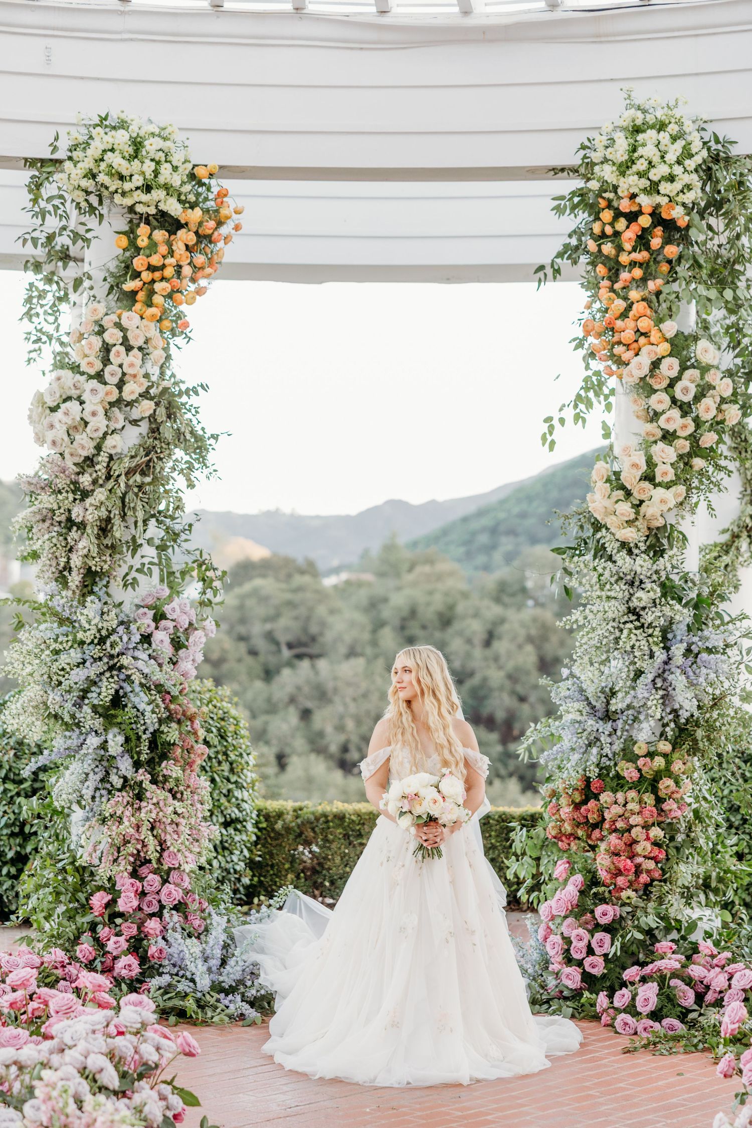 Wedding venue decorated with lush floral arches in pink, peach and white blooms overlooking mountain views.