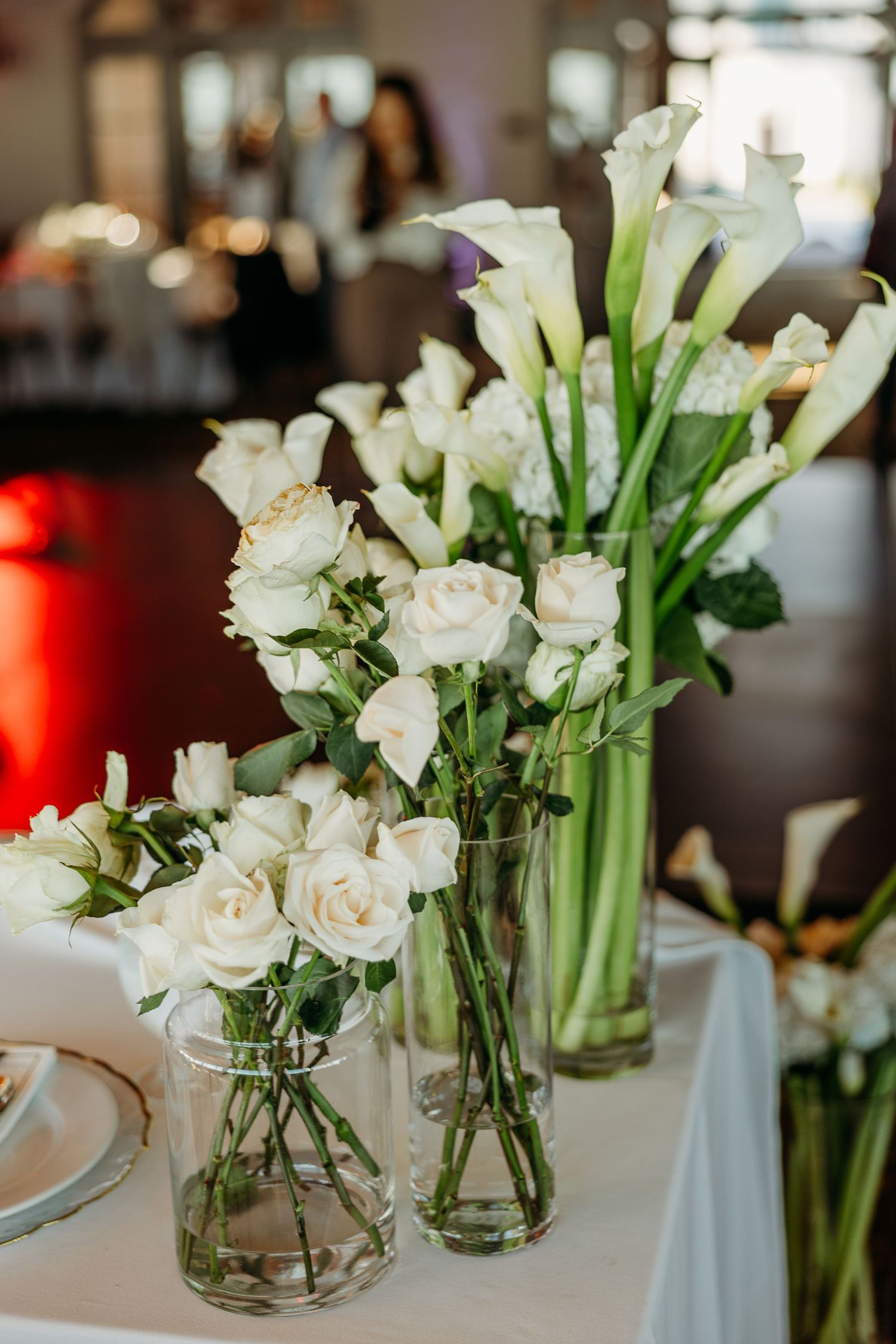 Elegant white calla lilies and roses arranged in clear glass vases on a wedding reception table.