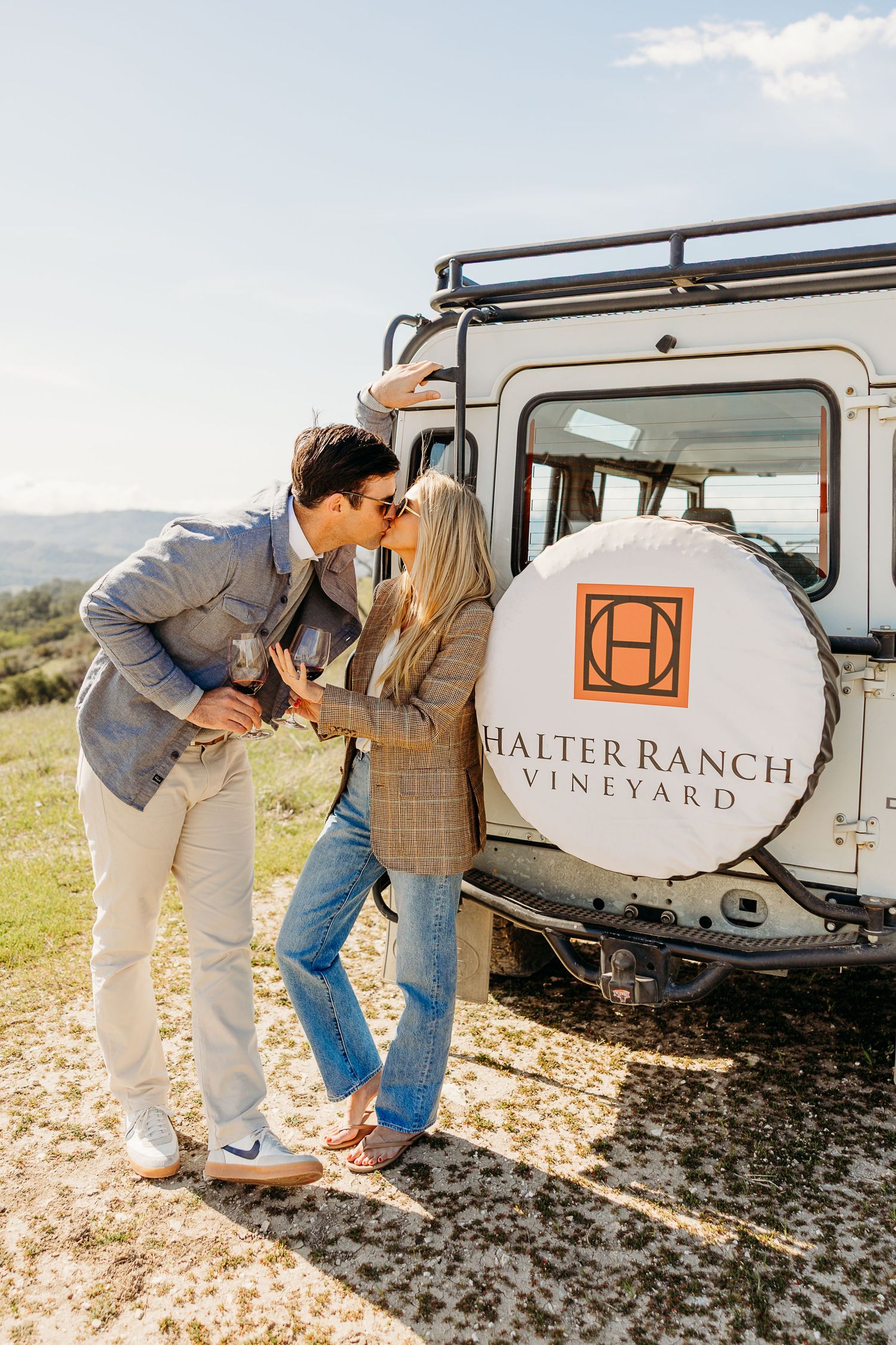 Two people share a romantic moment near a vineyard vehicle displaying Halter Ranch Vineyard branding.