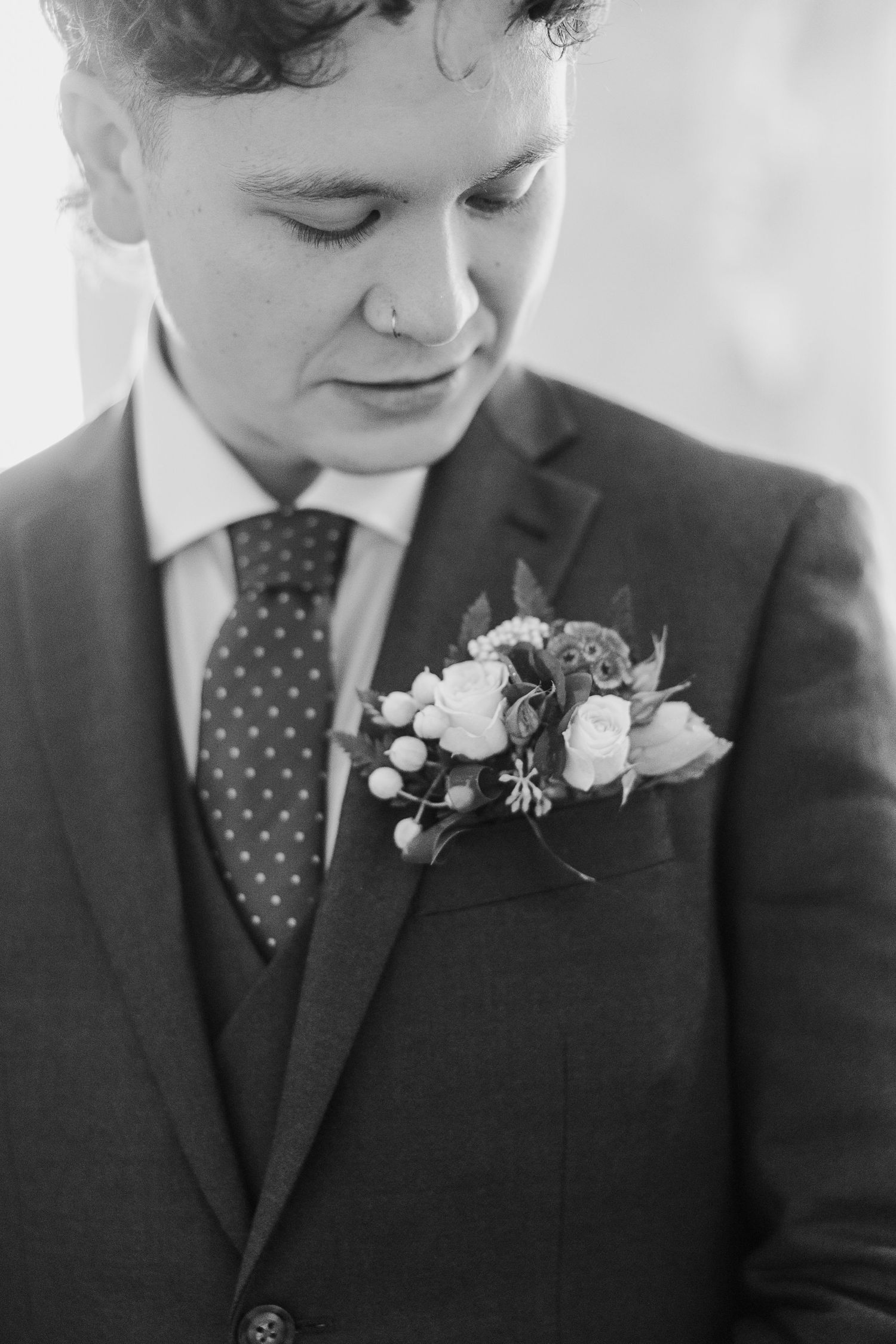 Close up details of a boutonniere with white flowers pinned to a dark suit jacket.