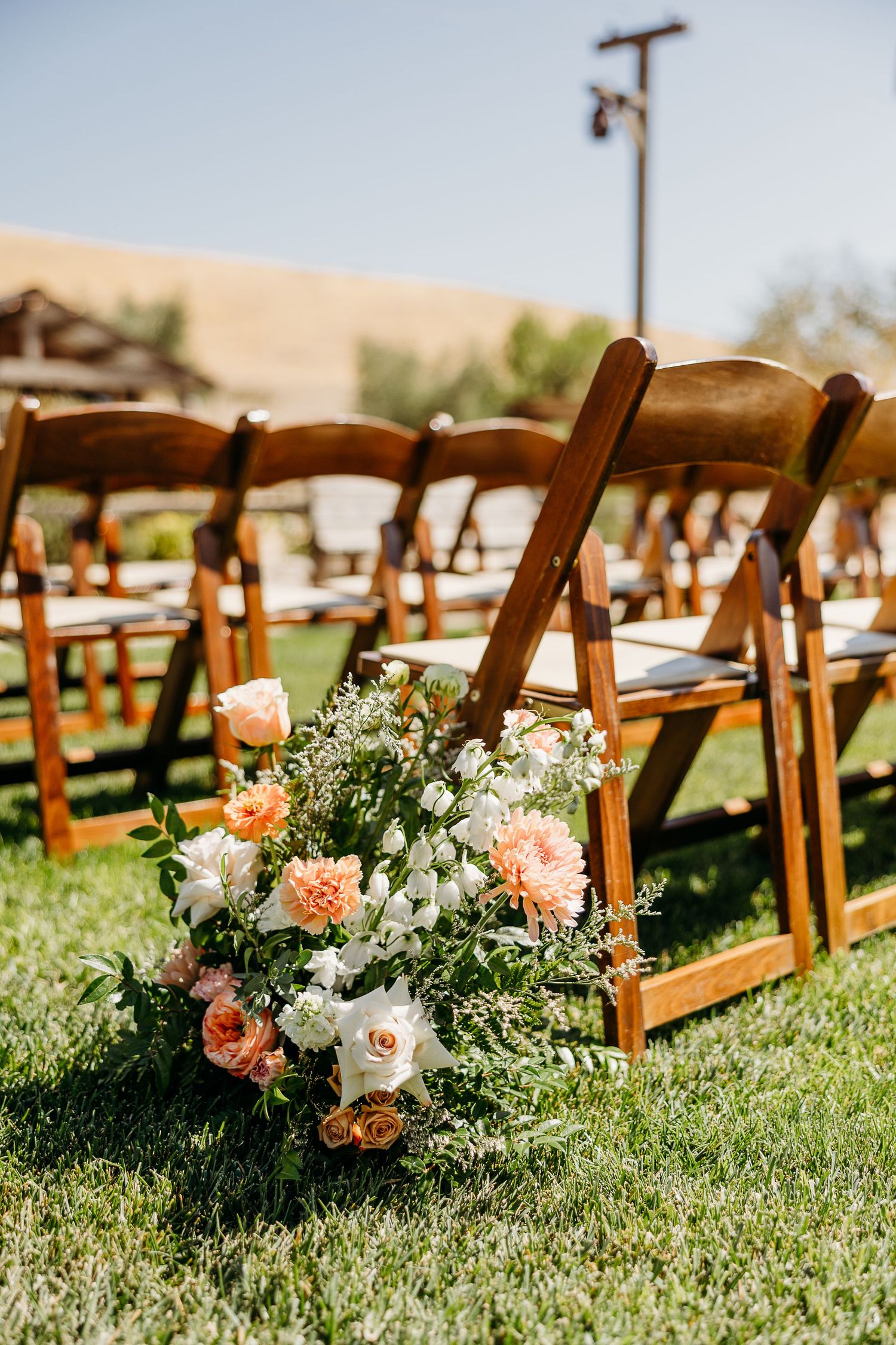 Wooden folding chairs with floral arrangements set up for outdoor wedding ceremony.
