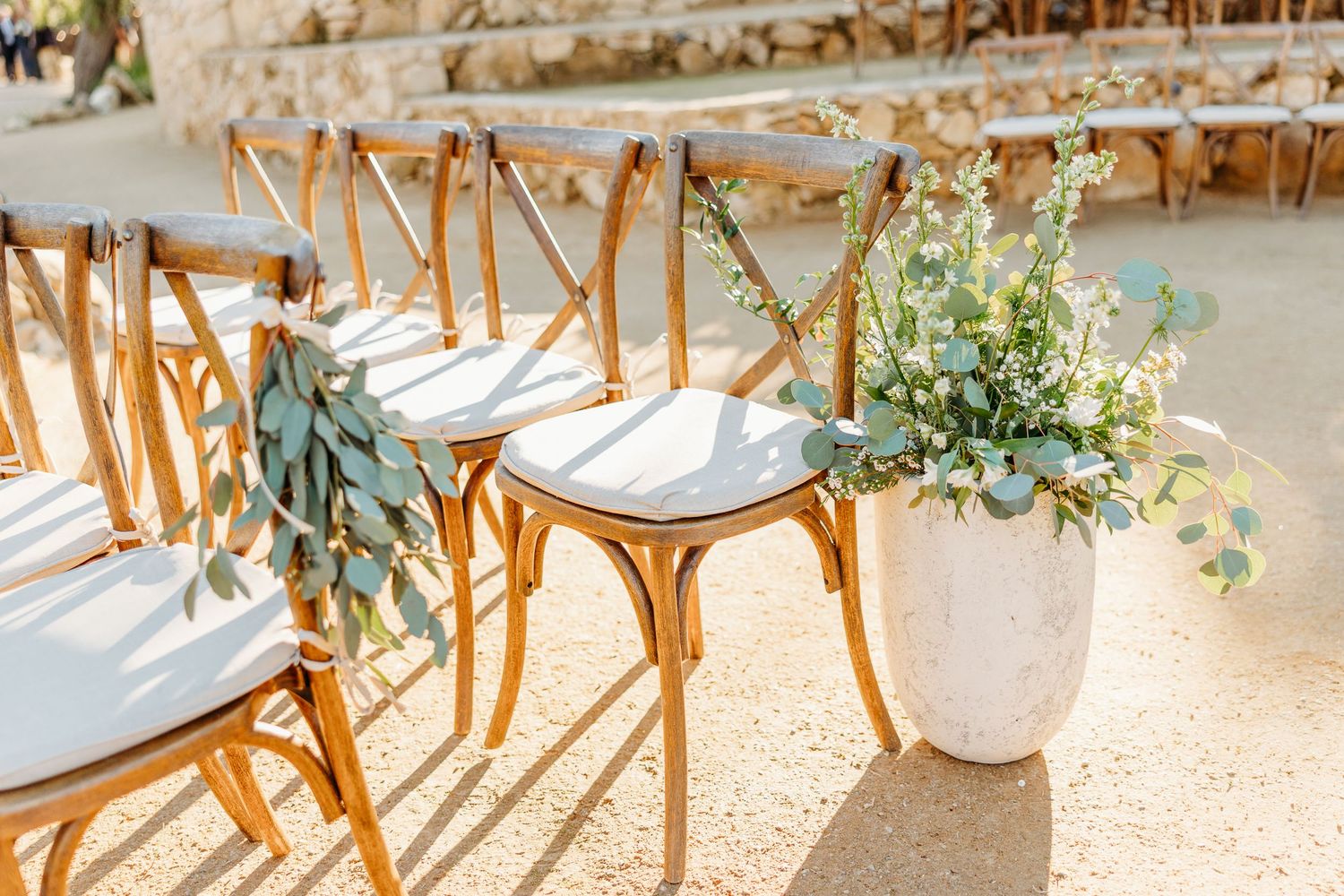 Elegant wedding reception table settings with wooden chairs and delicate greenery decorations in natural light.