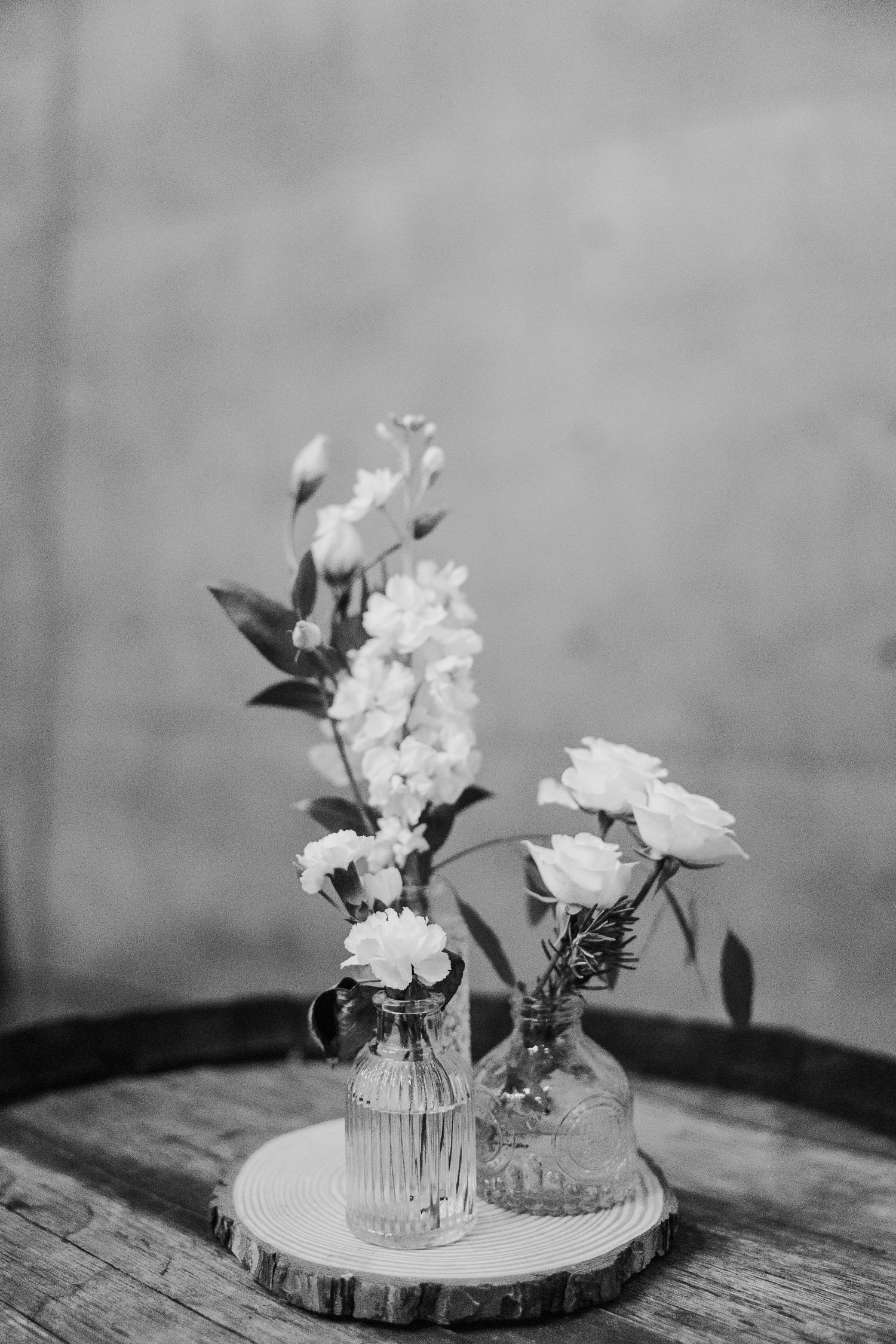 Black and white photo of delicate flowers arranged in vintage glass vases on a wooden surface.
