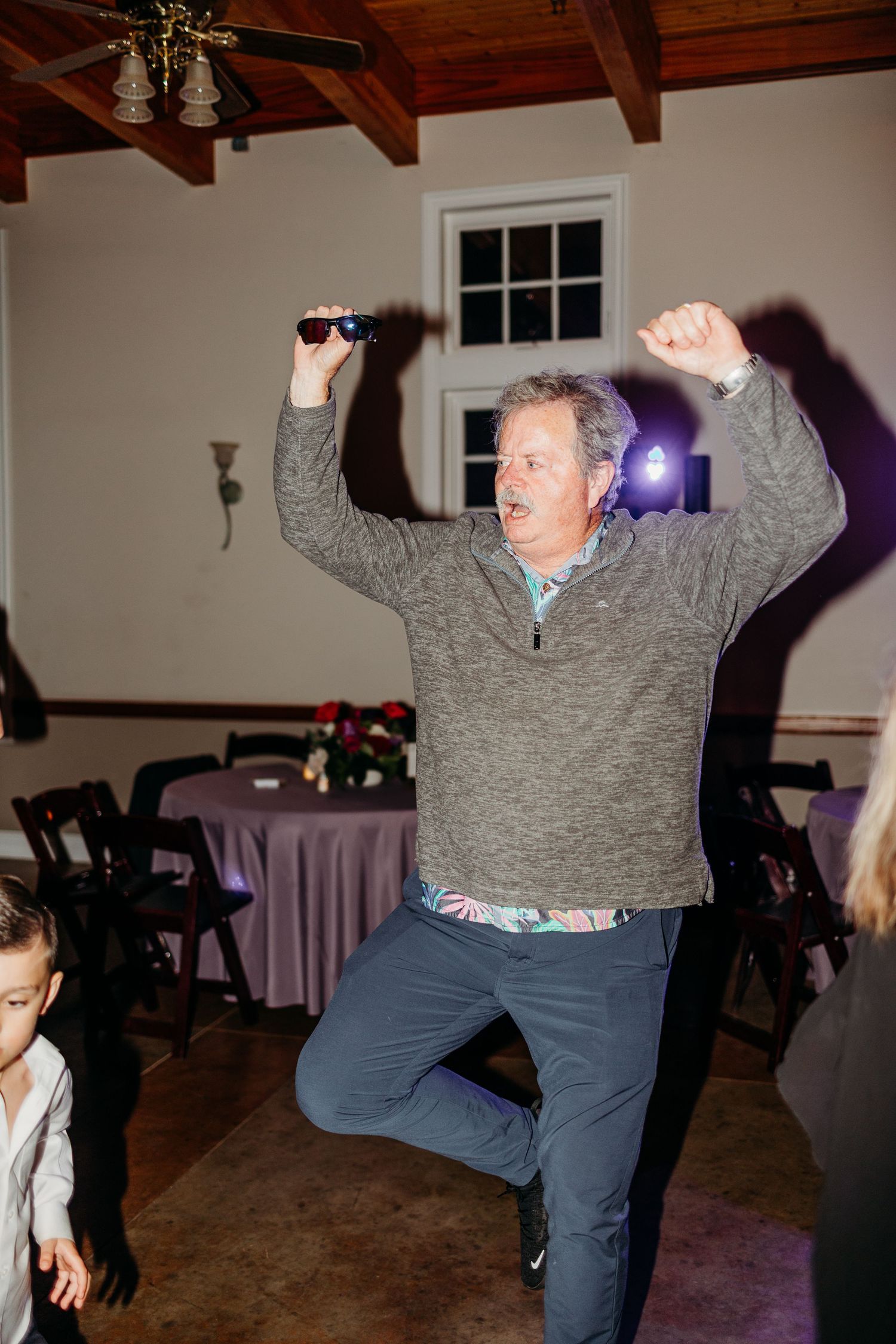 Wedding guest performing enthusiastic dance moves at indoor reception.