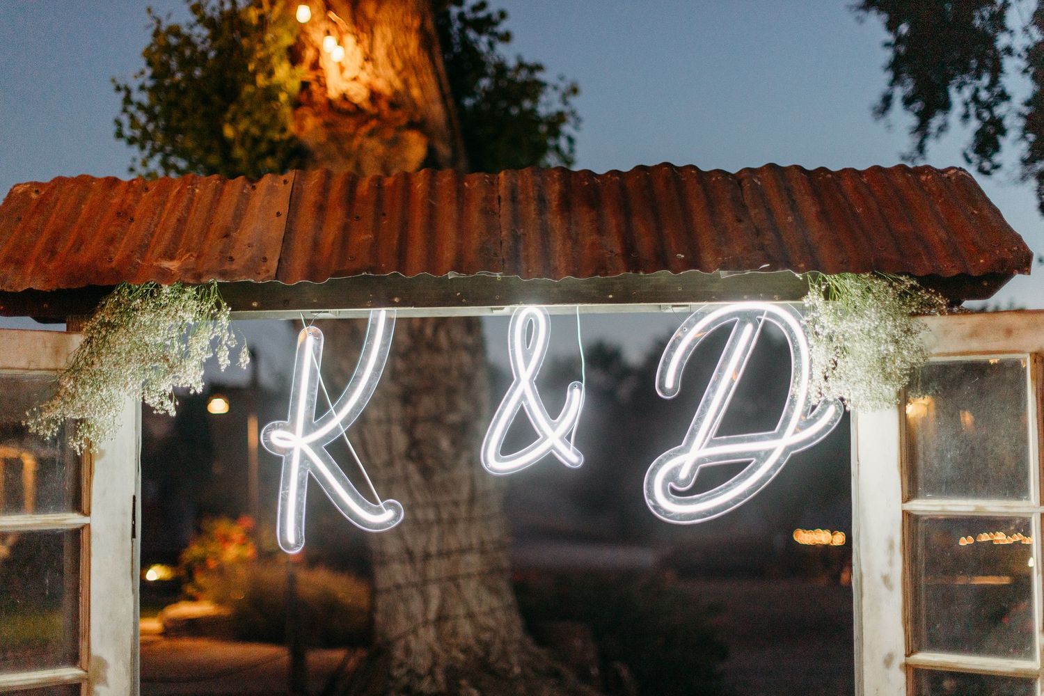 Illuminated neon wedding signage glows against a rustic barn backdrop at night.
