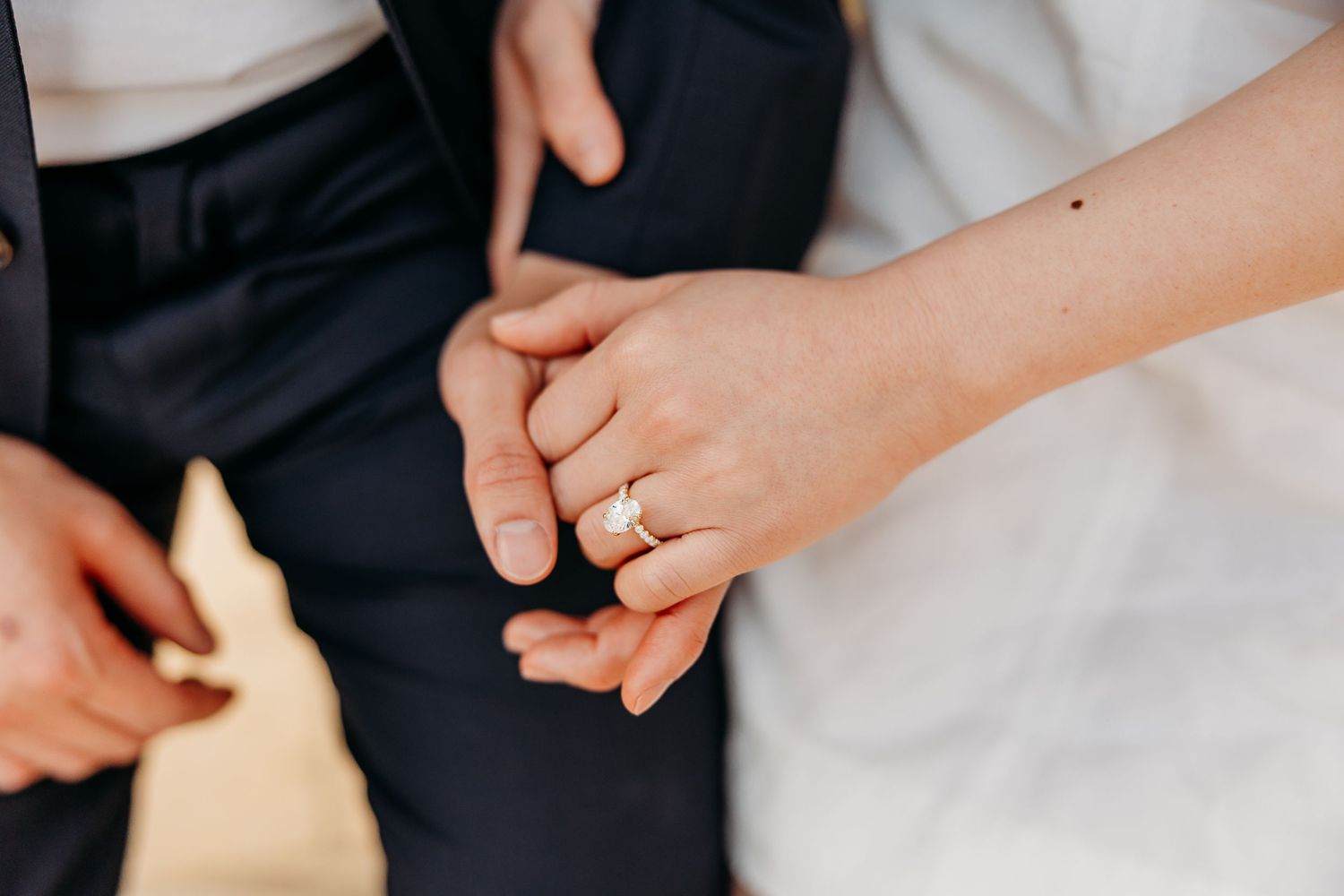 Close-up shot of hands with an engagement ring against formal attire.