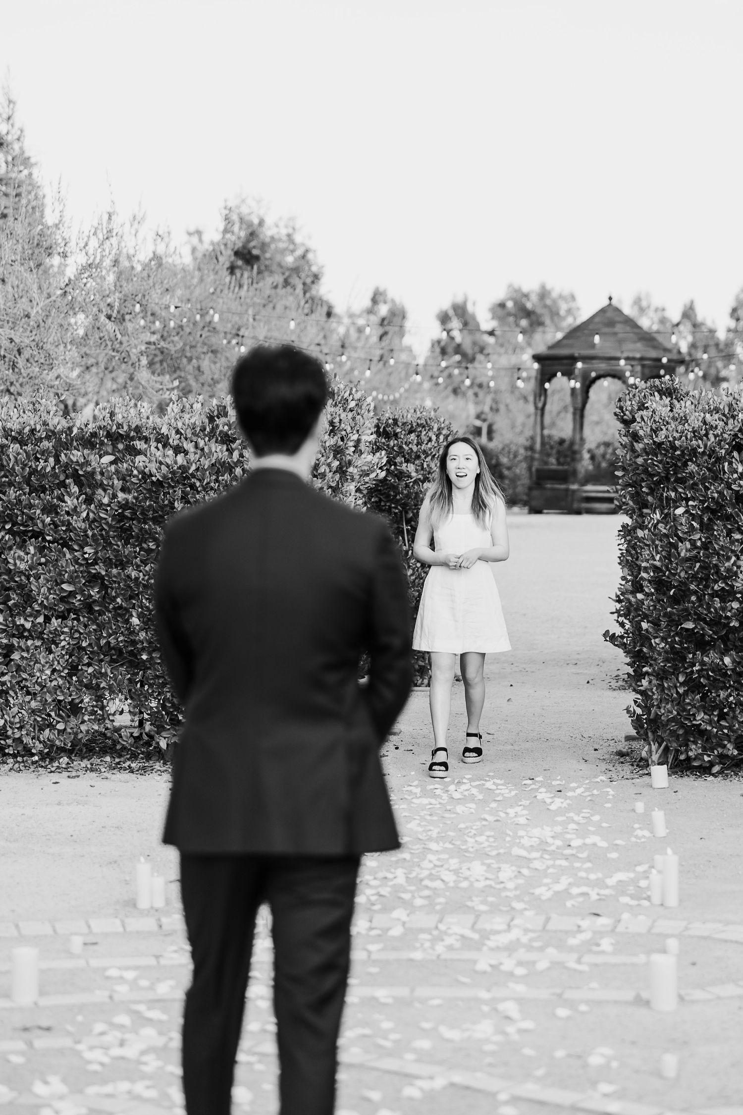 Black and white photo of a stone labyrinth path with hedges and trees in the background.