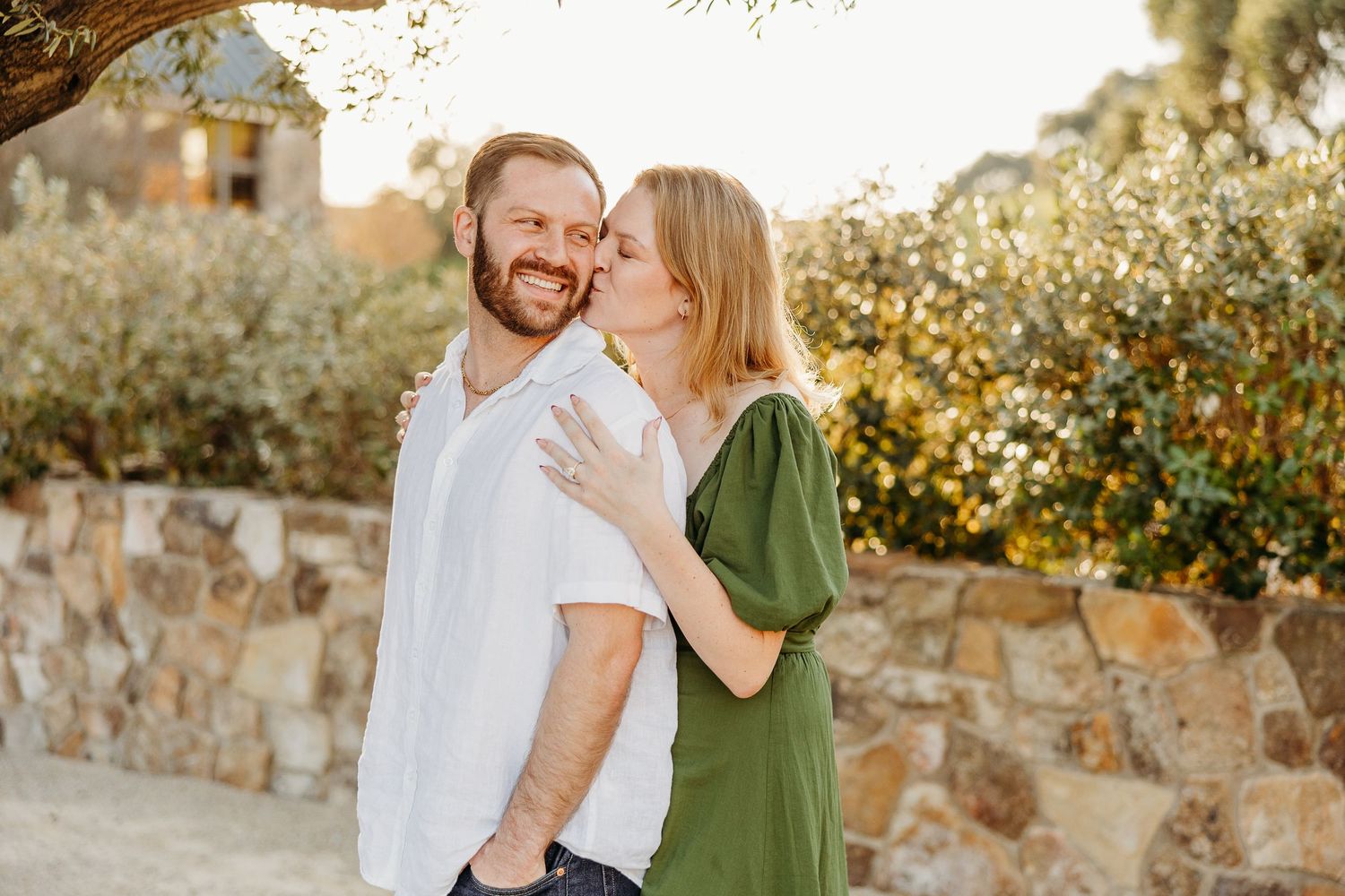 Affectionate couple shares tender moment against rustic stone wall in garden setting.