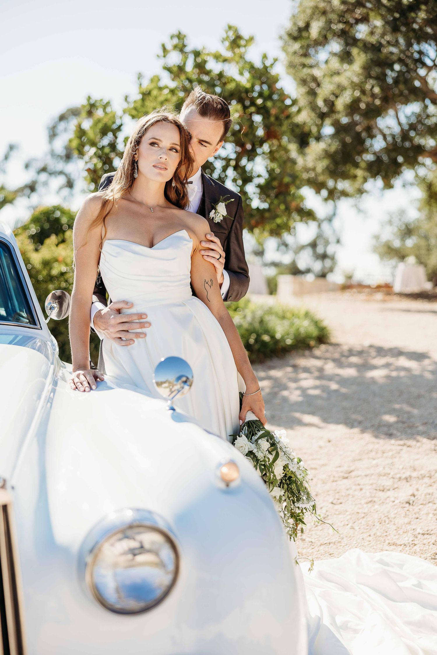 Romantic wedding photos taken with a classic white car in bright sunlight.