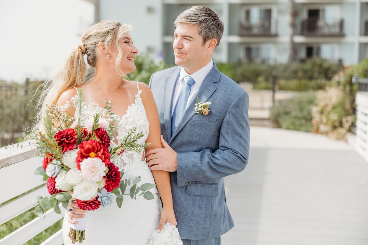 Elegant seaside wedding portrait with vibrant red and white bouquet.