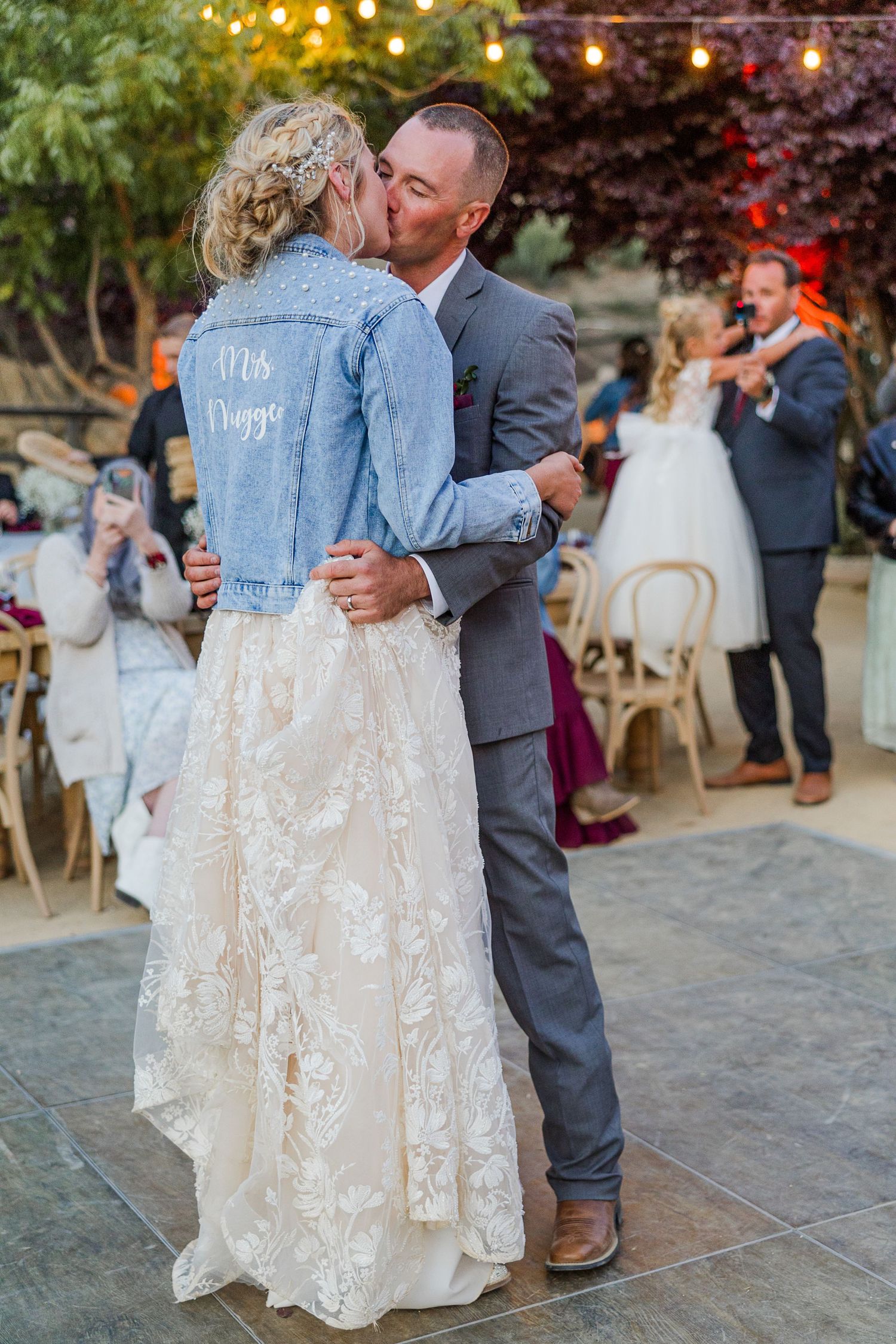 Couple dancing at reception with bride wearing customized denim jacket over lace wedding dress.