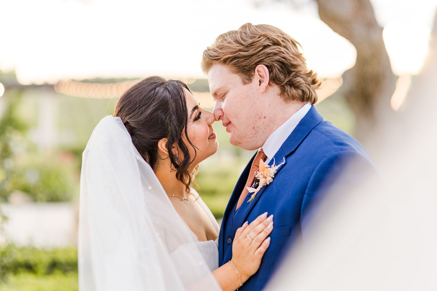 A tender moment between newlyweds sharing an intimate kiss in a sunlit garden.