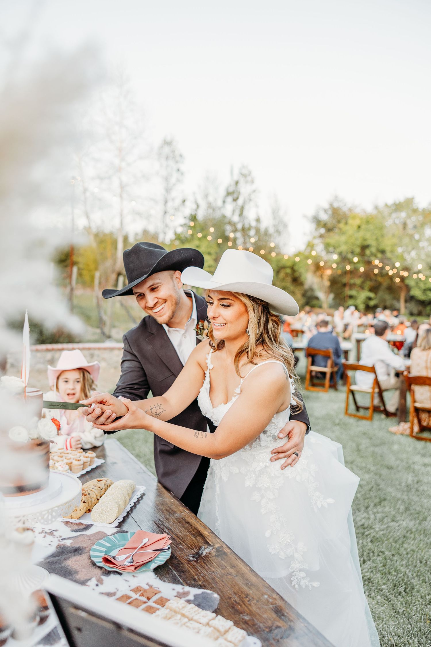 Newlyweds in cowboy hats sharing a moment at their rustic outdoor reception.