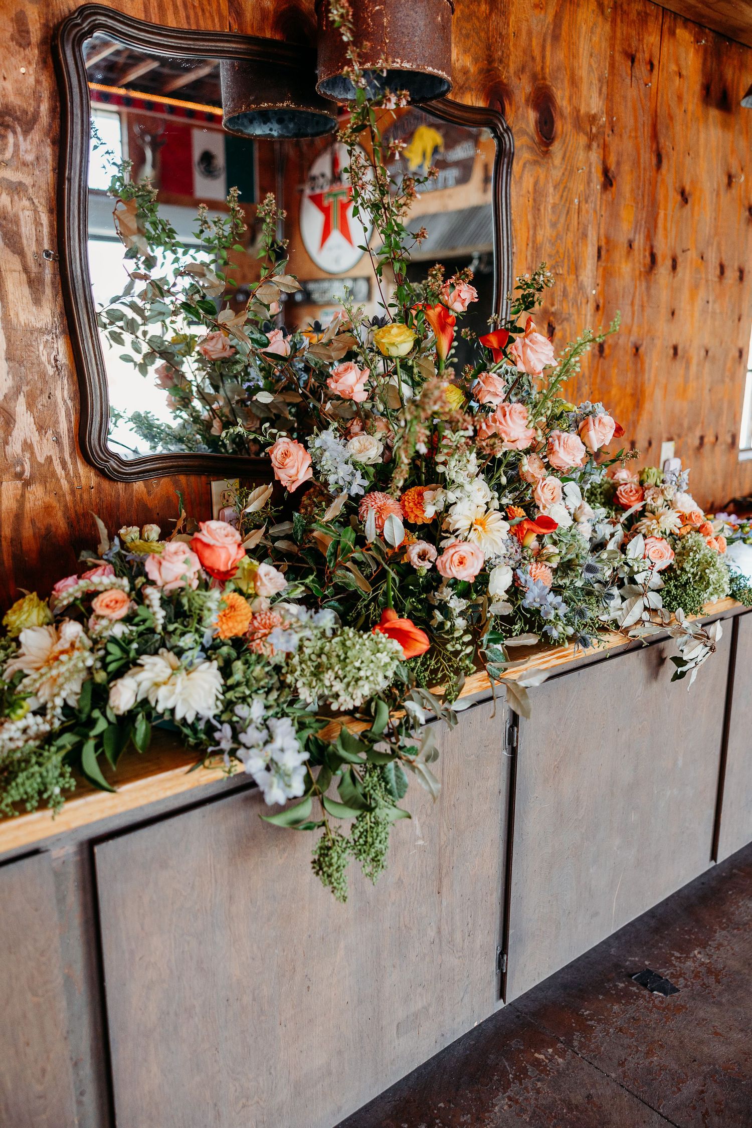 Elegant floral arrangement with pink roses and greenery displayed on wooden cabinet with ornate mirror.