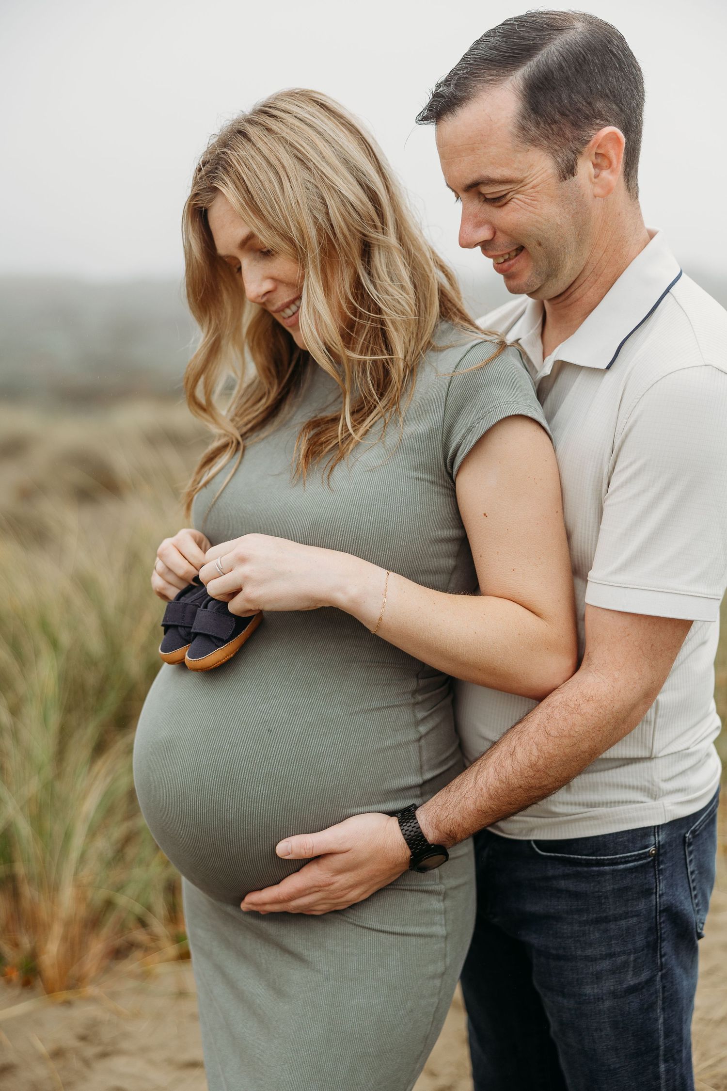 Tender maternity moment captured as couple holds baby shoes against growing bump.